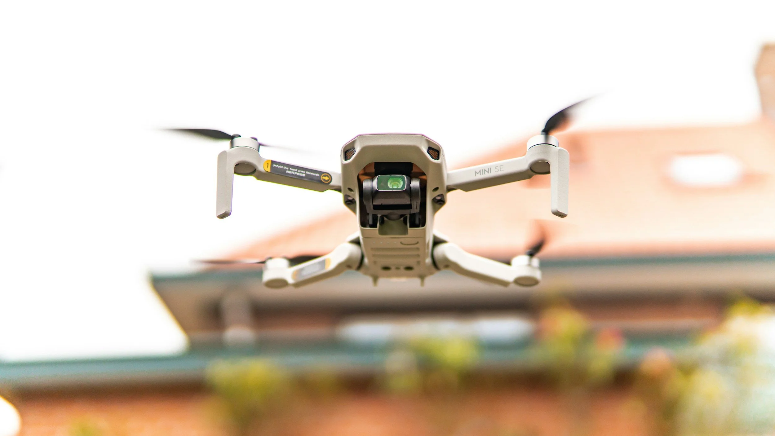 A drone flying outdoors near a building with a white sky in the background.