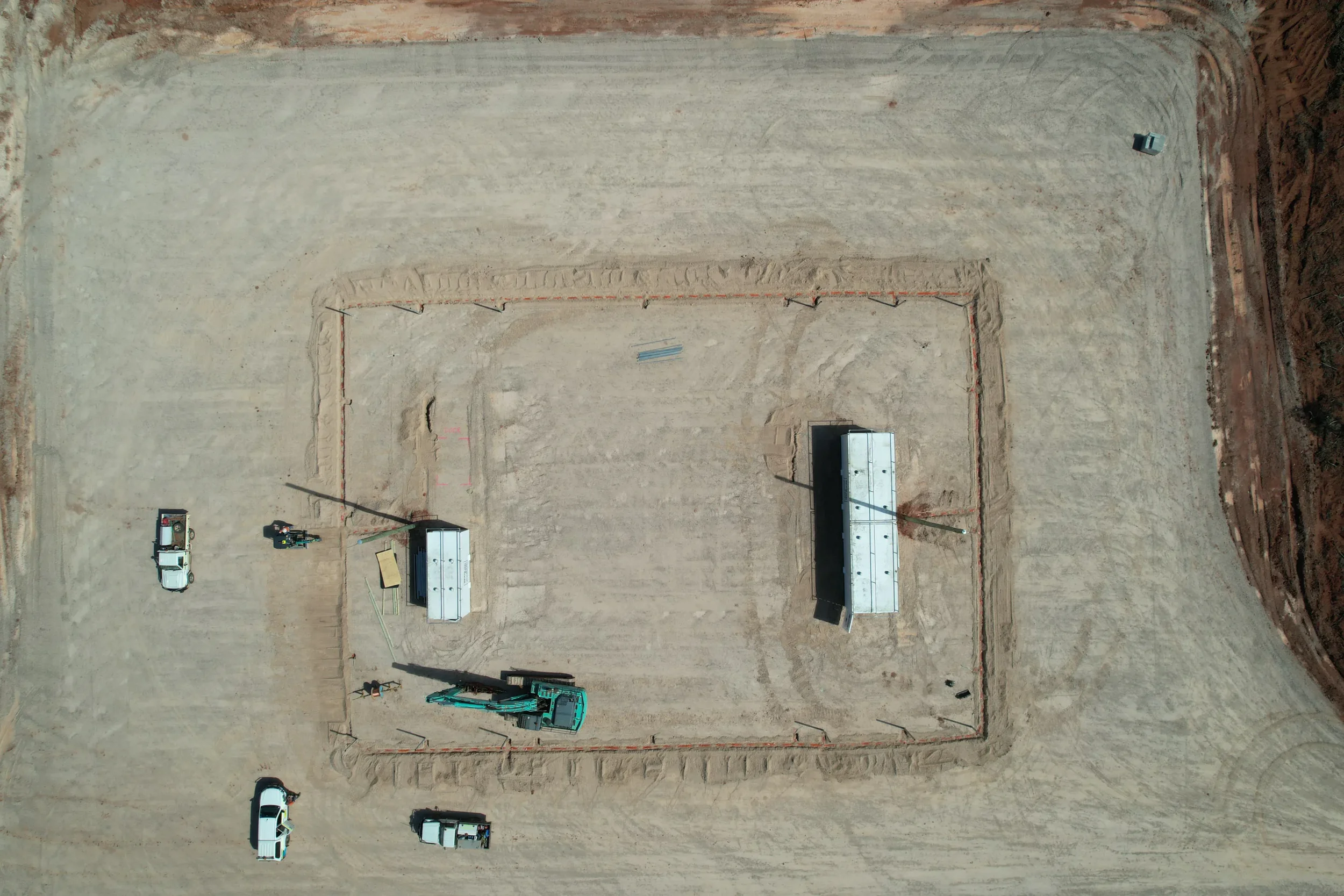 An aerial view of a construction site with a leveled dirt area, construction vehicles, and equipment.