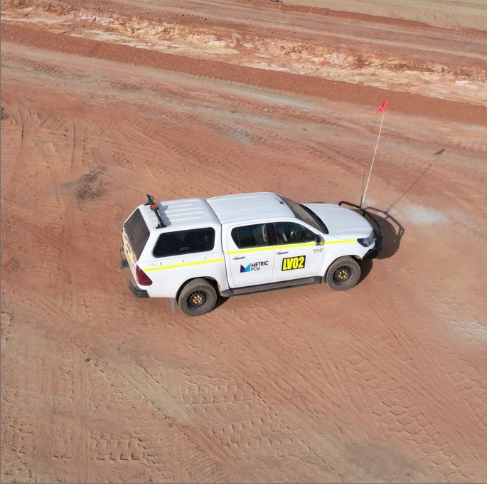 An off-road vehicle with a white body, yellow markings, and antennas on a dirt road, marked with the labels 'LV02' and 'METRIC'.