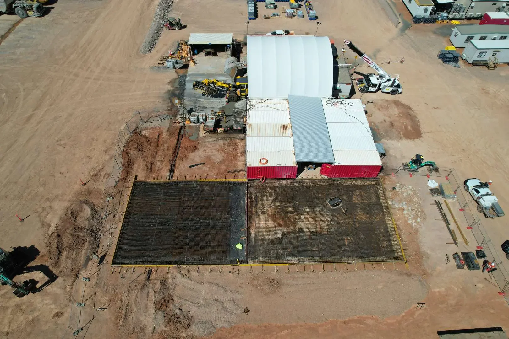 Aerial view of a construction site with various equipment, vehicles, and partially constructed structures on a dirt lot.
