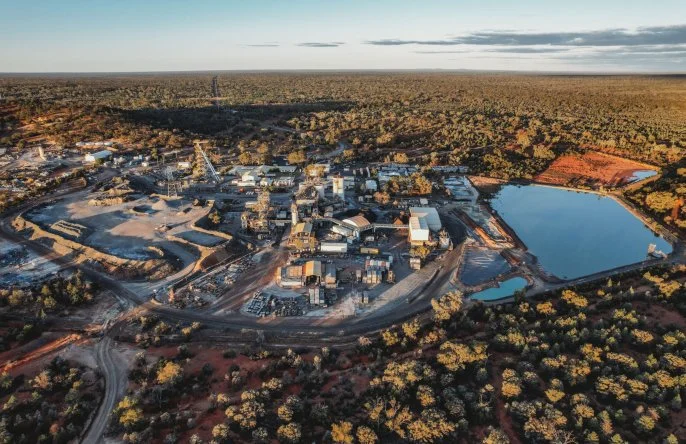 Aerial view of an industrial complex with buildings, roads, and water bodies surrounded by forest.