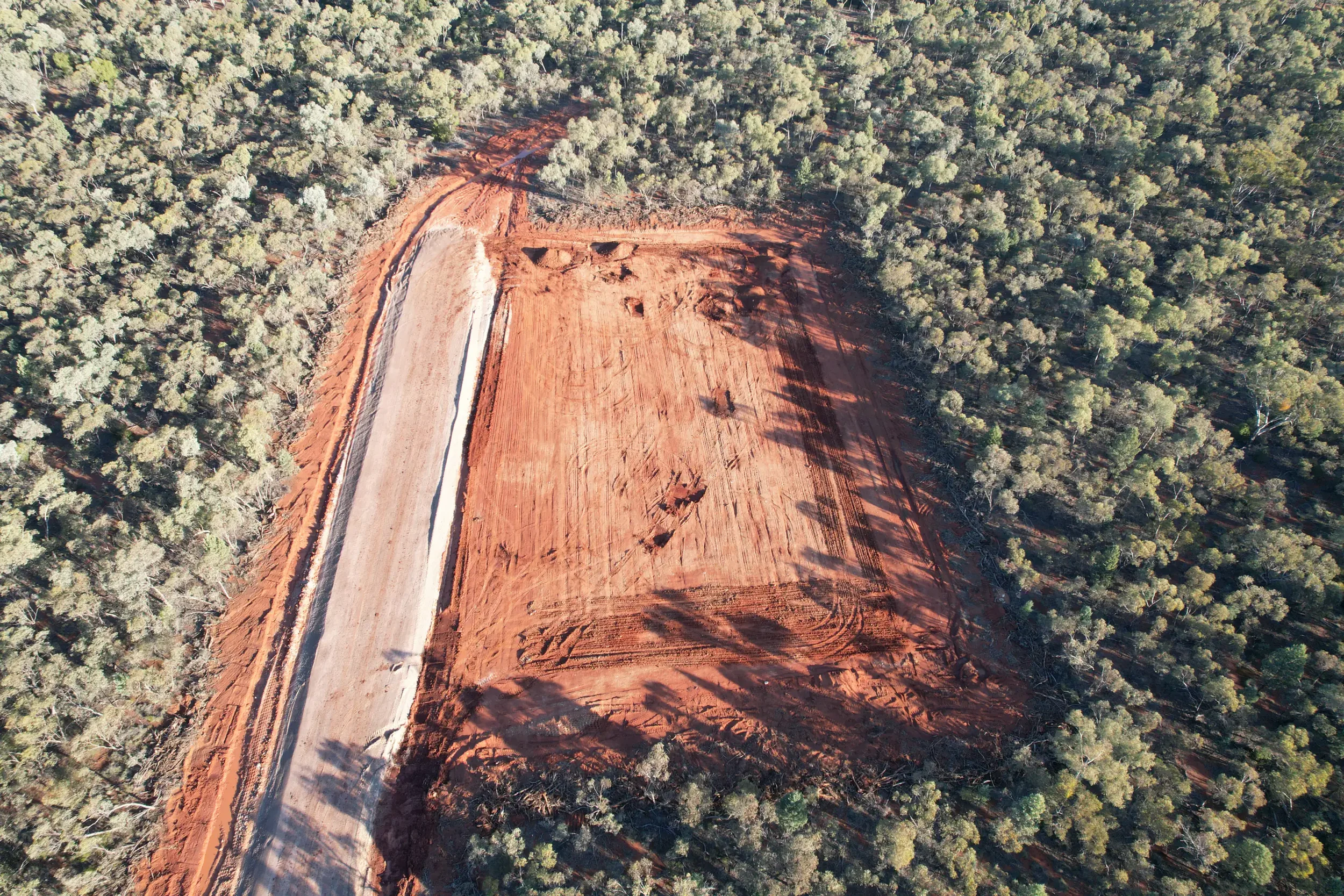 An aerial view of a forest with a cleared construction site and a road running through it.