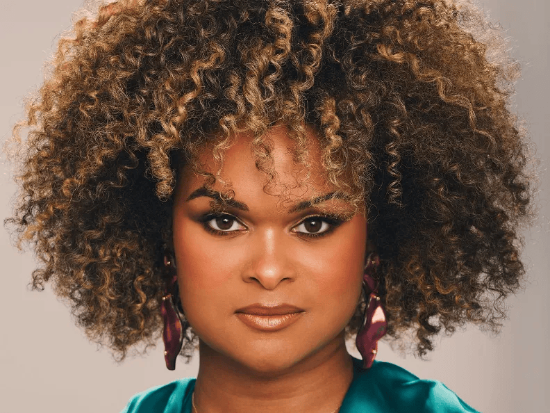 A woman with voluminous curly hair, wearing bold makeup and statement earrings.