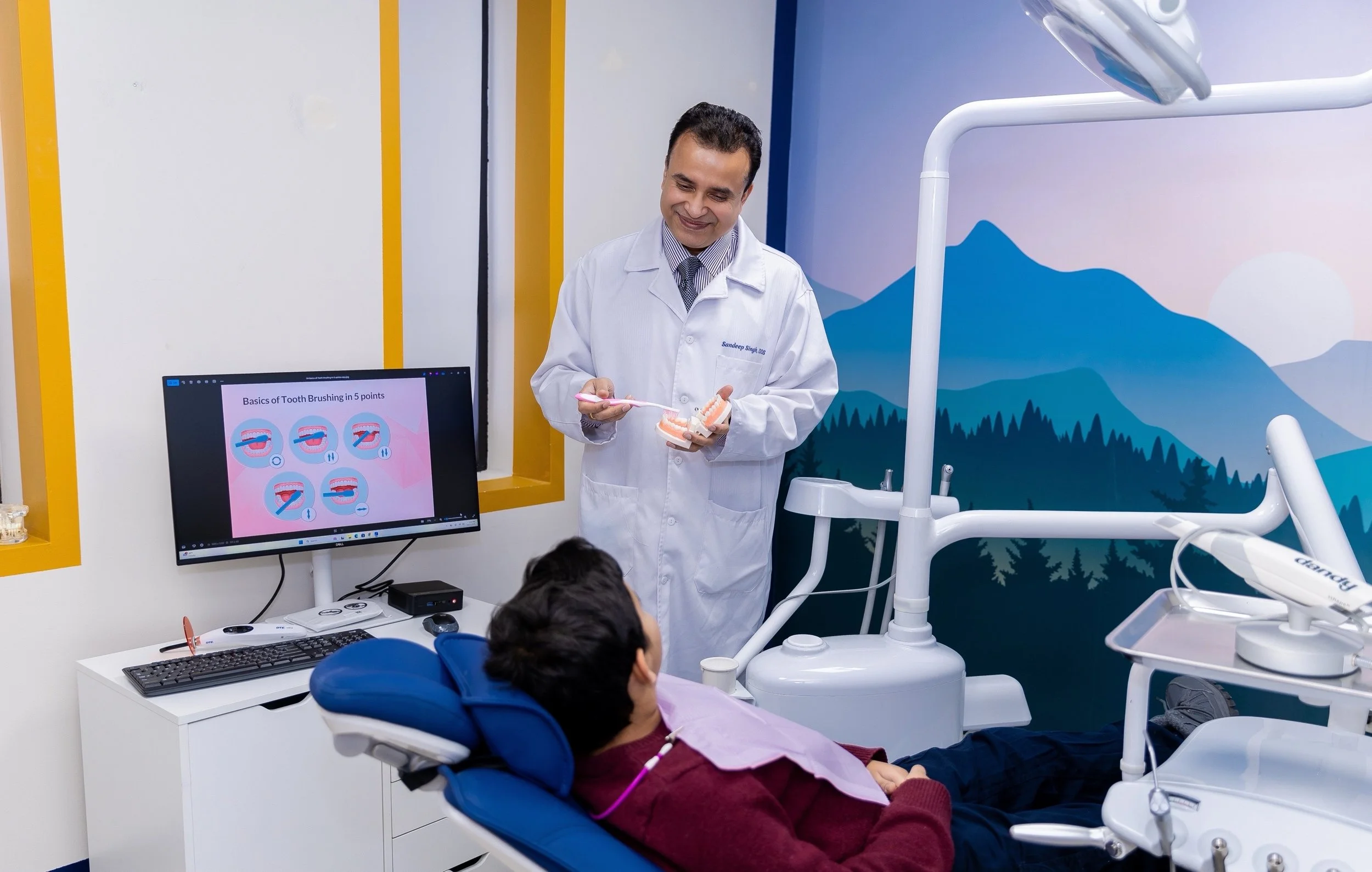 Dr. Singh showing dental model to patient in dental clinic with educational display on teeth brushing.