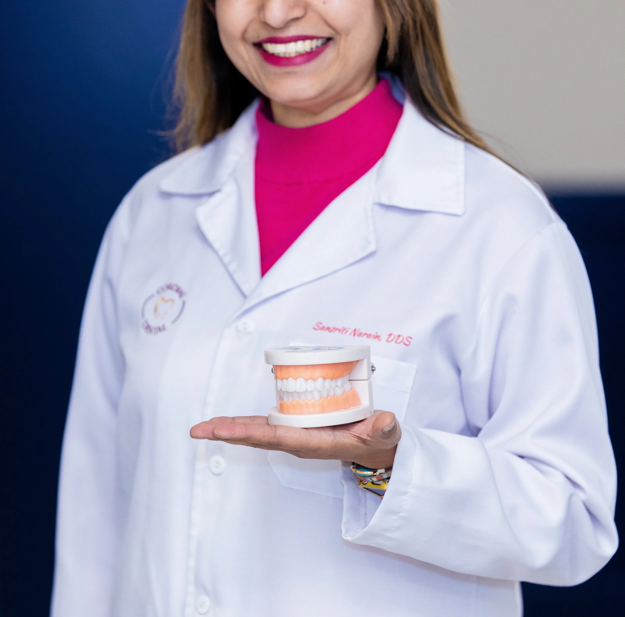 Dr. Narain in a white medical coat holding a model of human teeth.
