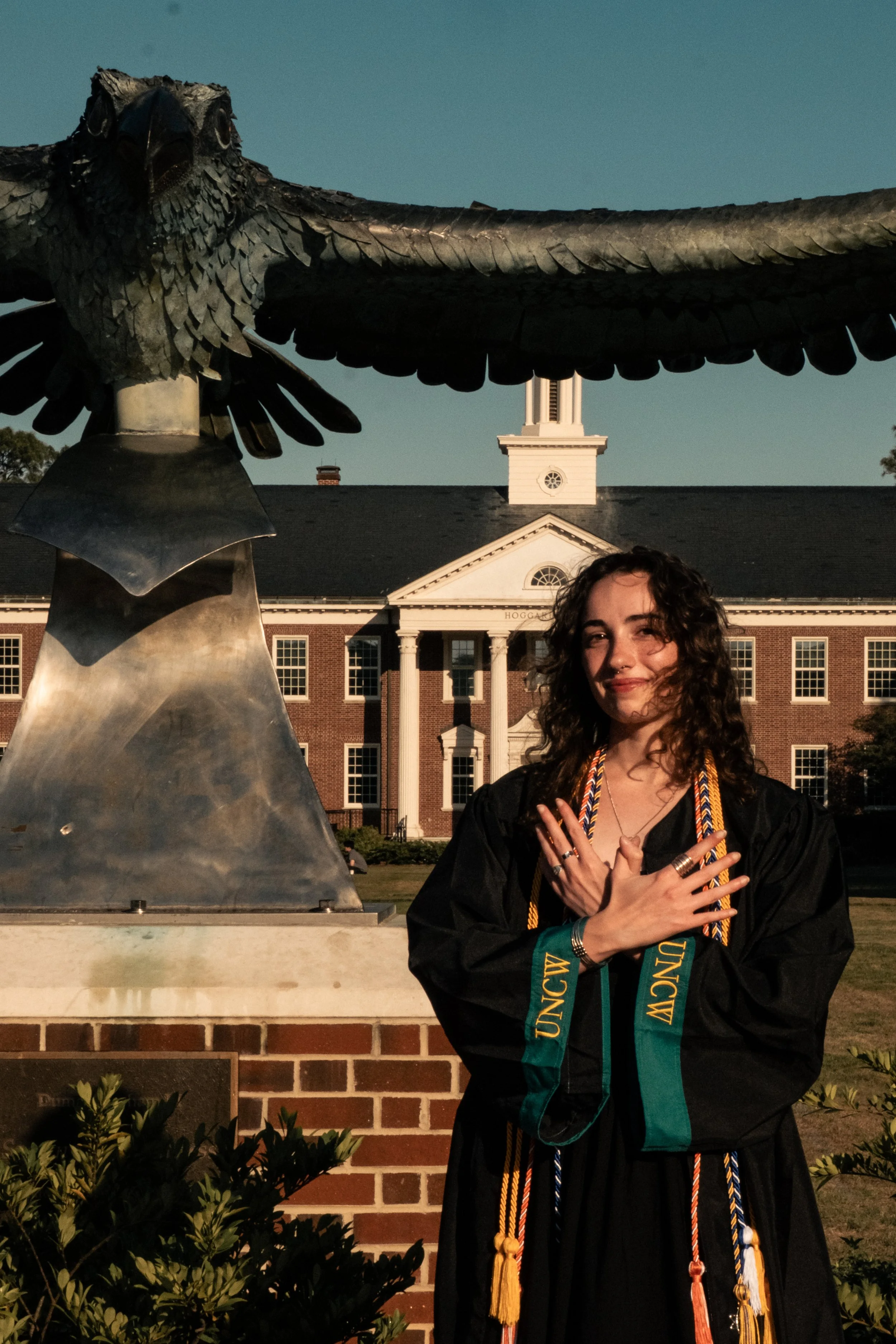 Young woman in graduation gown and cords standing in front of a building with a statue of an eagle with outstretched wings.