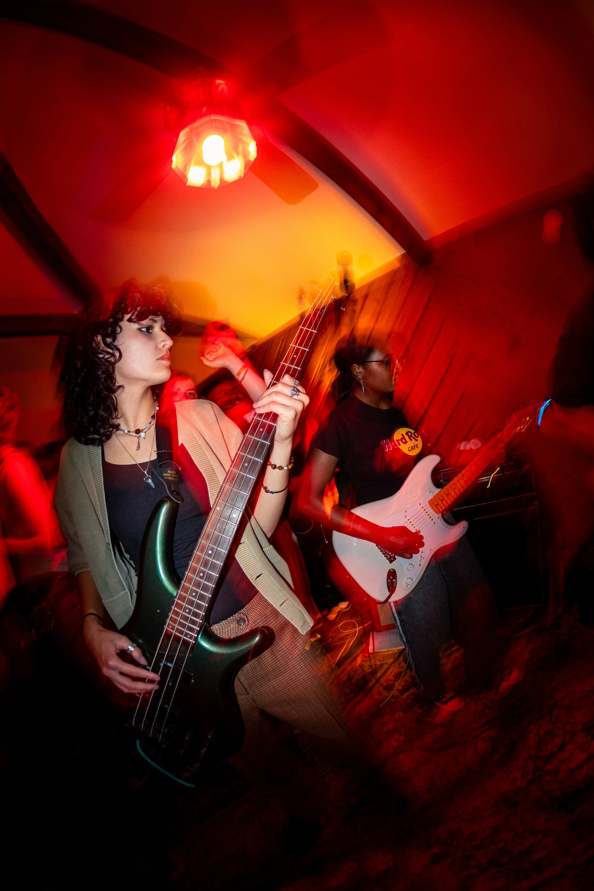 Two women playing electric guitars at a dimly lit music venue with red lighting.