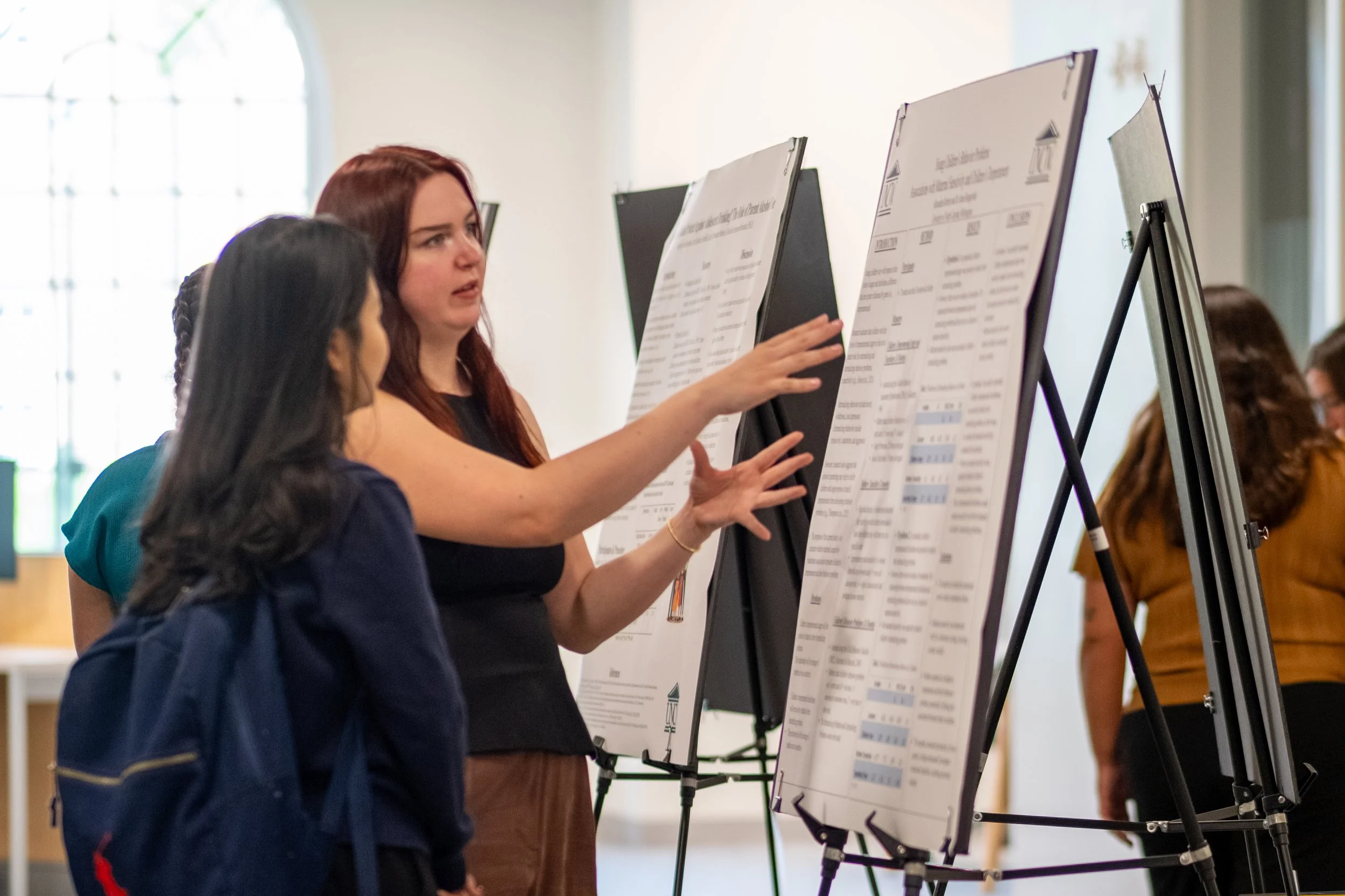Women talking and looking at display boards with charts and data in a bright room.