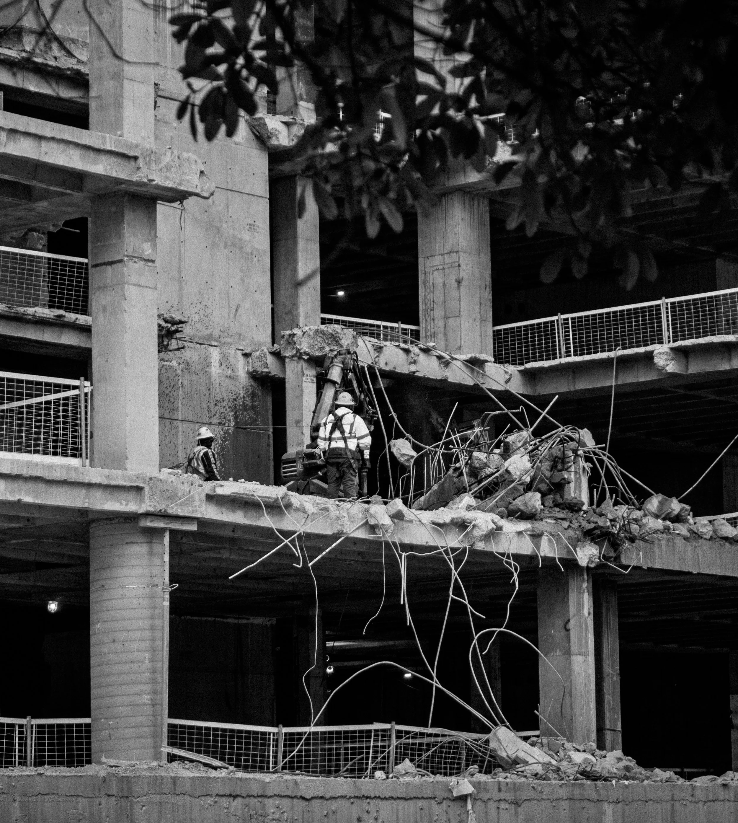 Construction workers working on a demolition under a bridge, with debris and exposed rebar.