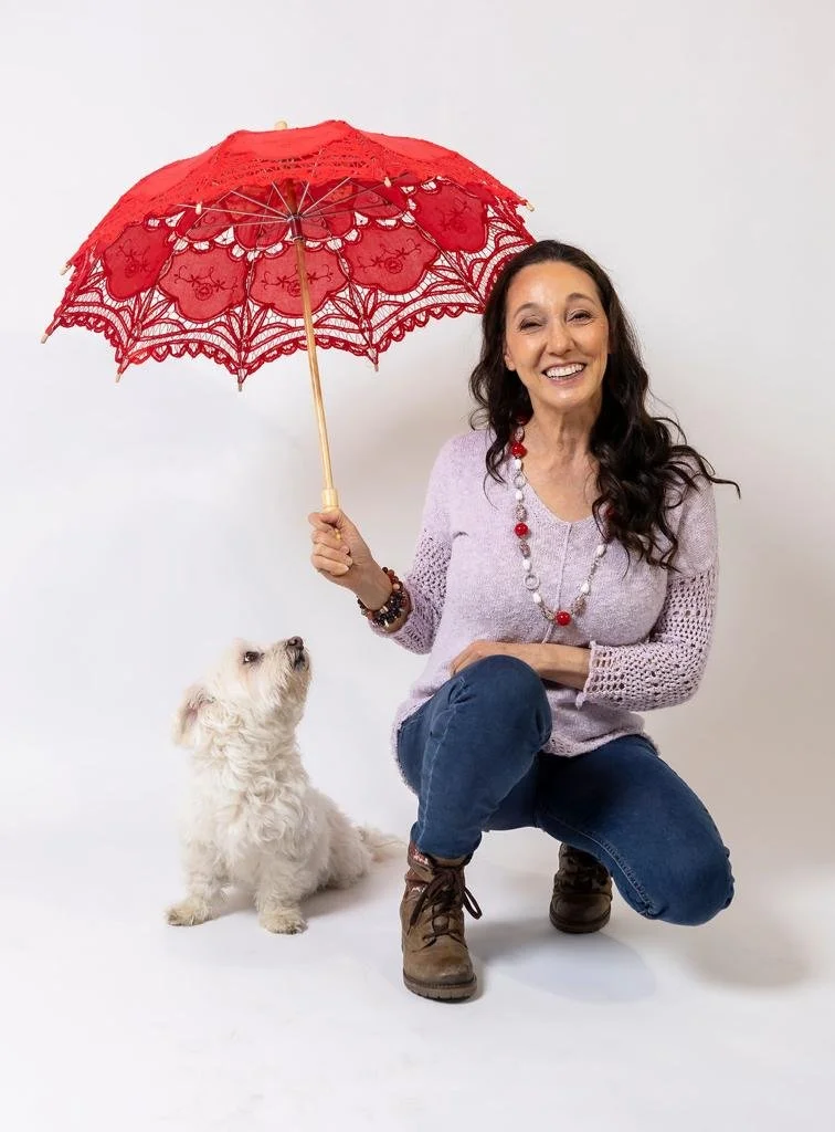 Alessandra kneeling and smiling, holding a red lace parasol, with a small white dog sitting beside her.