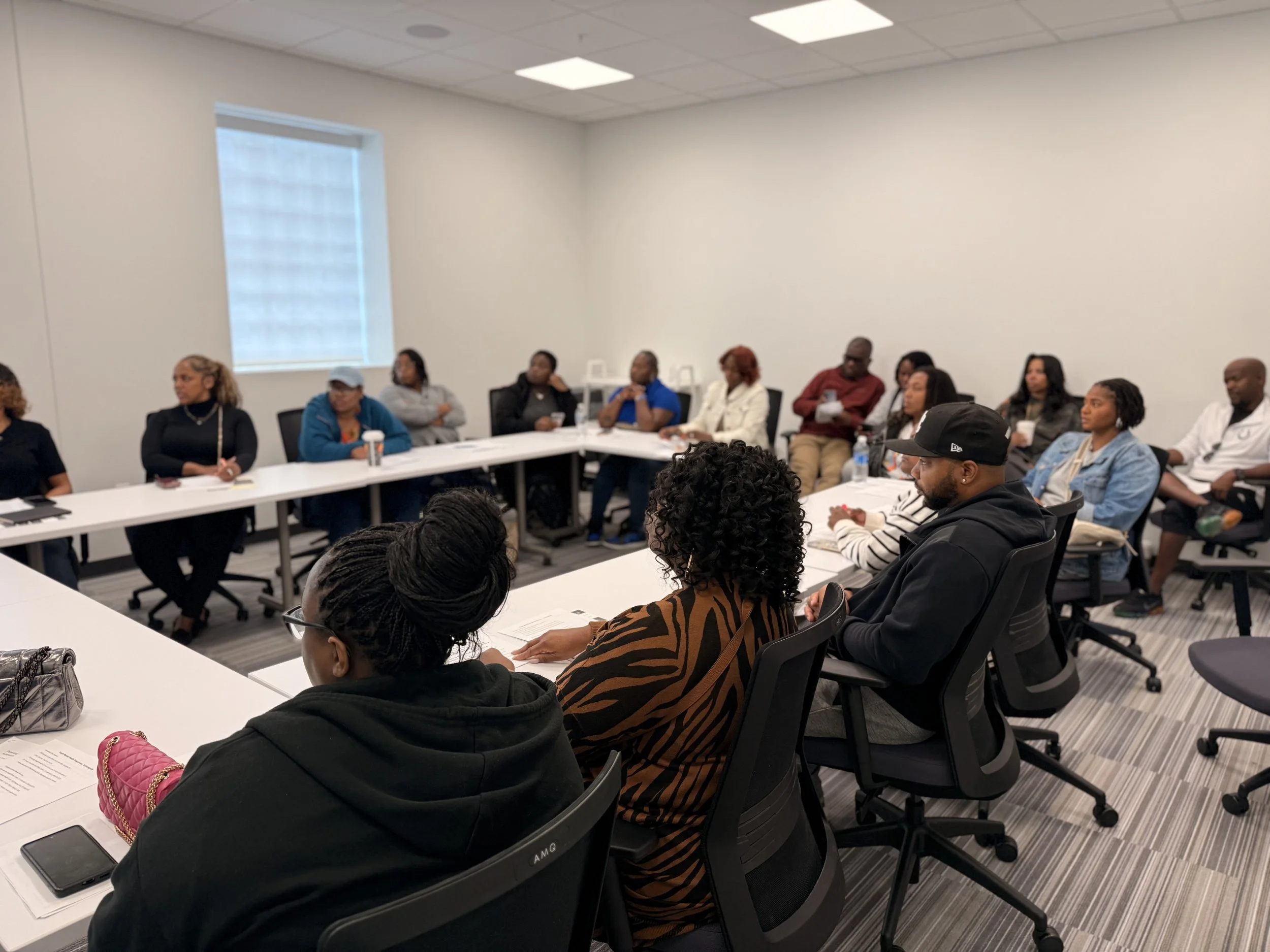 A diverse group of people sitting around a large rectangular table in a conference room, engaged in a meeting or discussion.