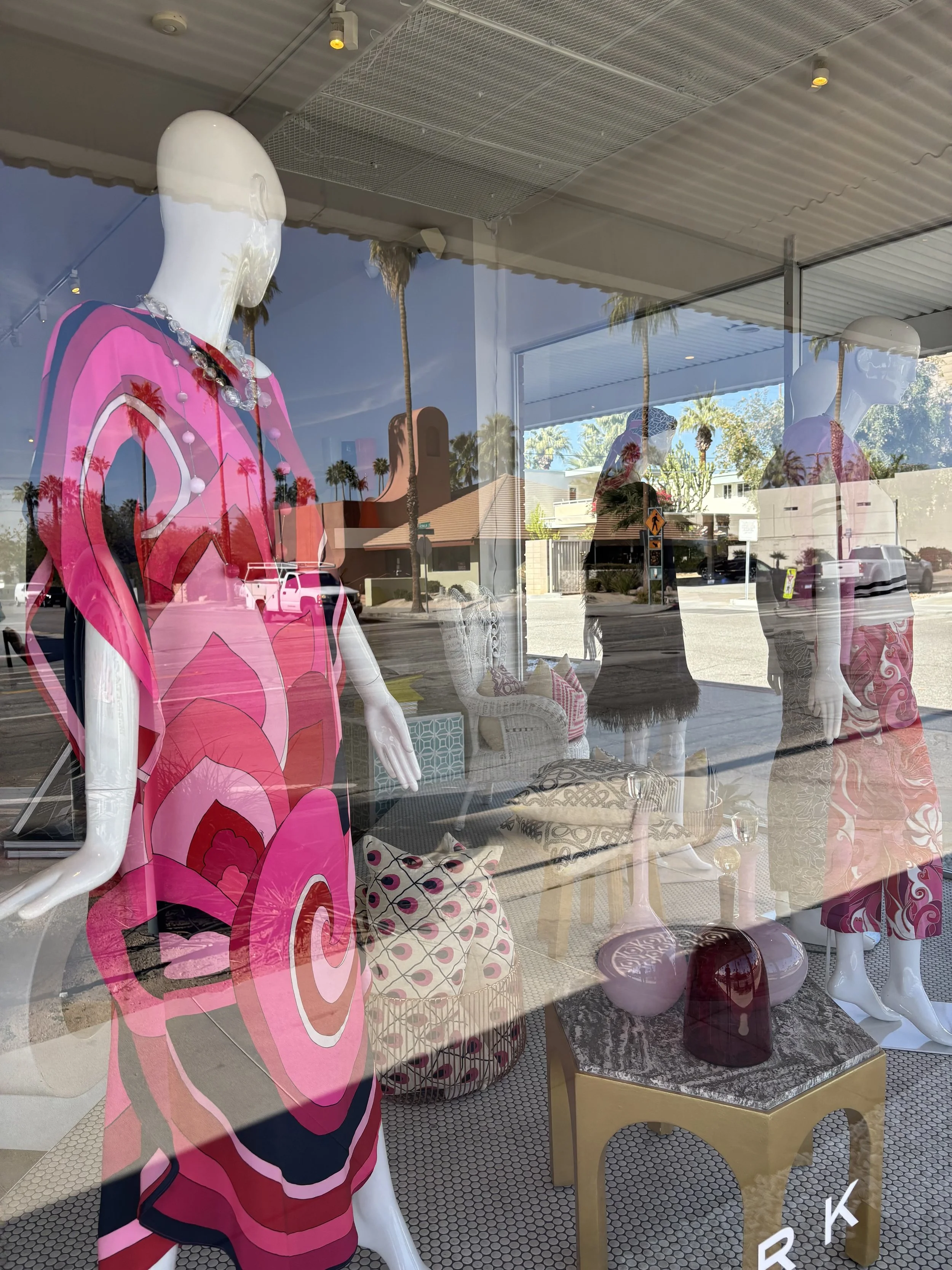 A storefront with large glass window is displaying a brightly colored dress on a mannequin.