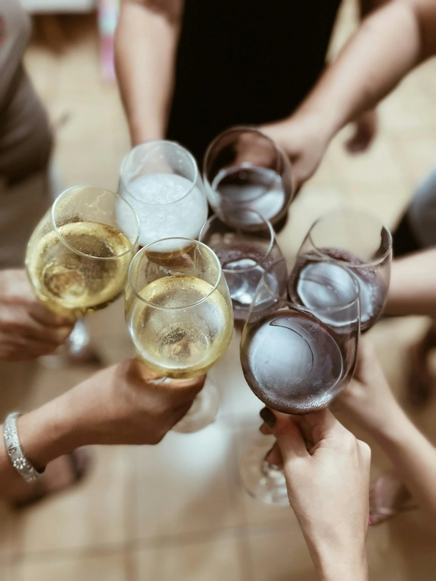 People toasting with glasses of champagne and red wine with their arms outstretched while touching the glasses.