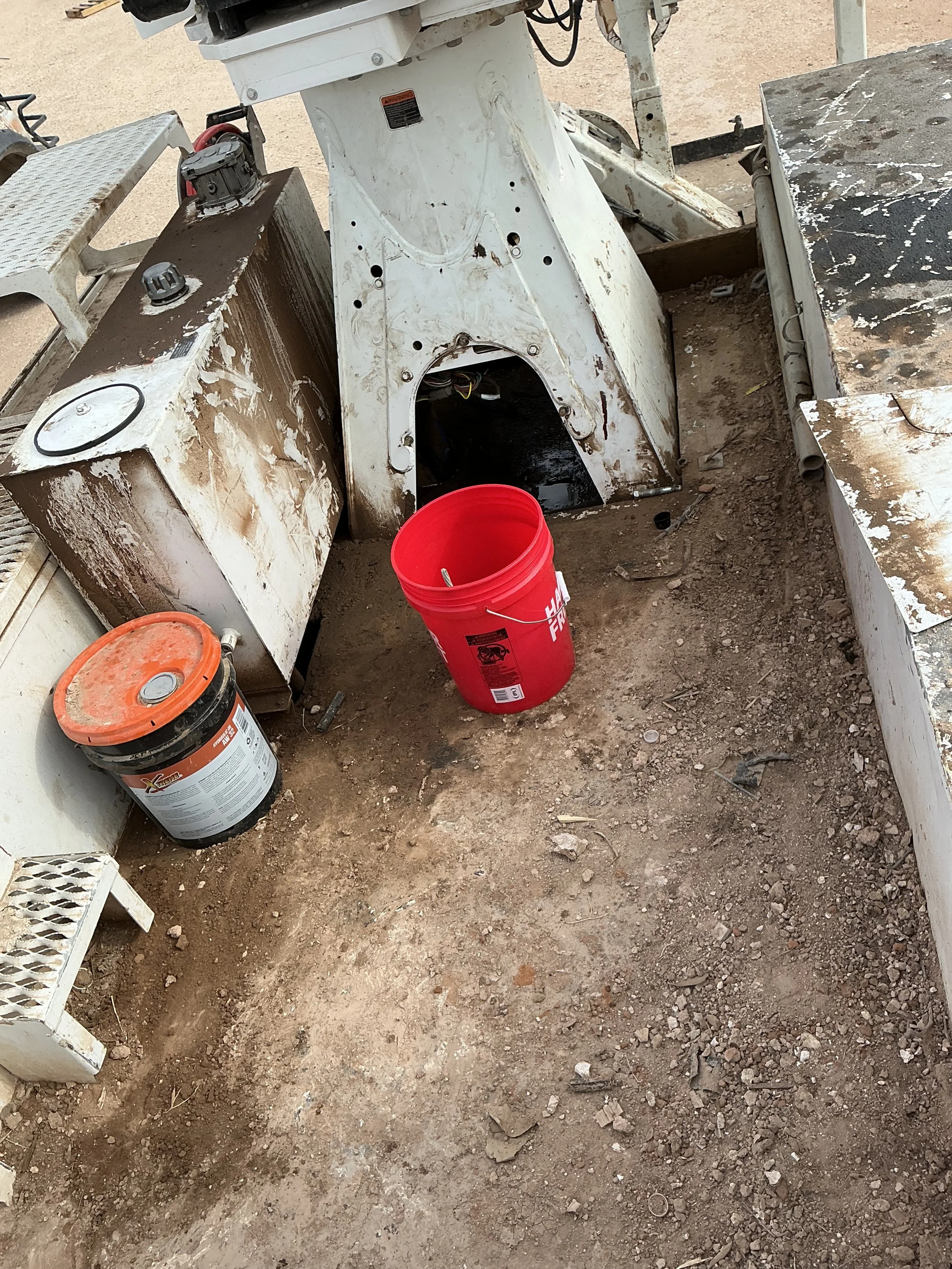 Disassembled construction equipment on dirt ground, with red and black buckets and surrounding tools.