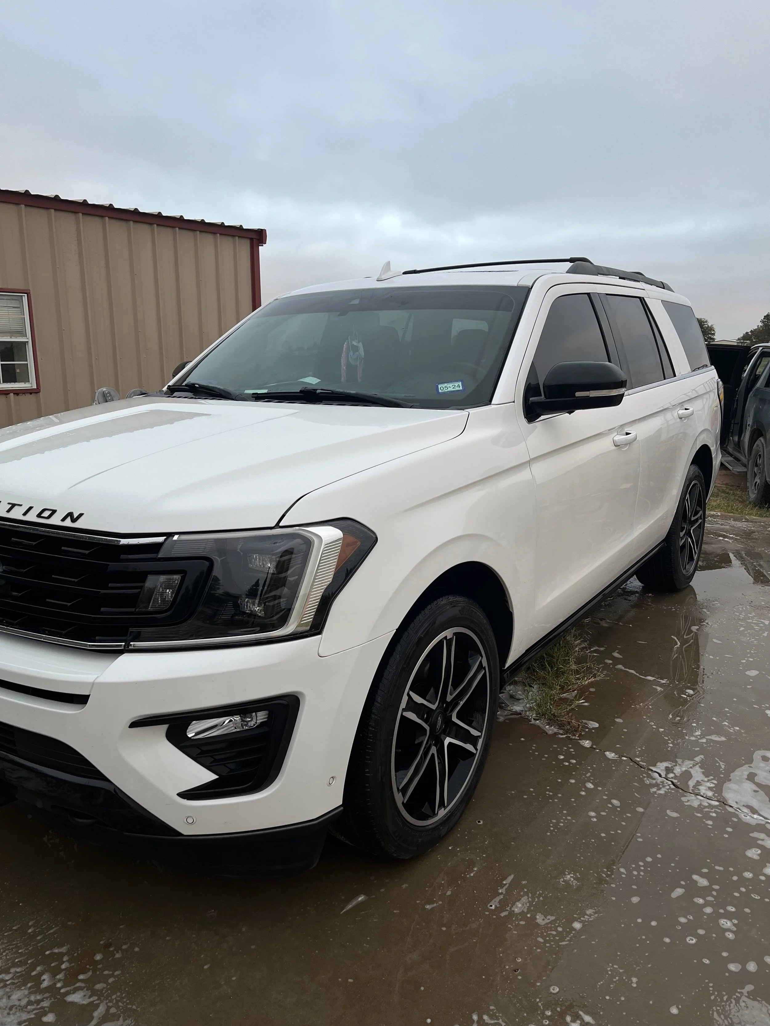 White SUV parked on wet ground next to a beige building with red trim under cloudy sky.