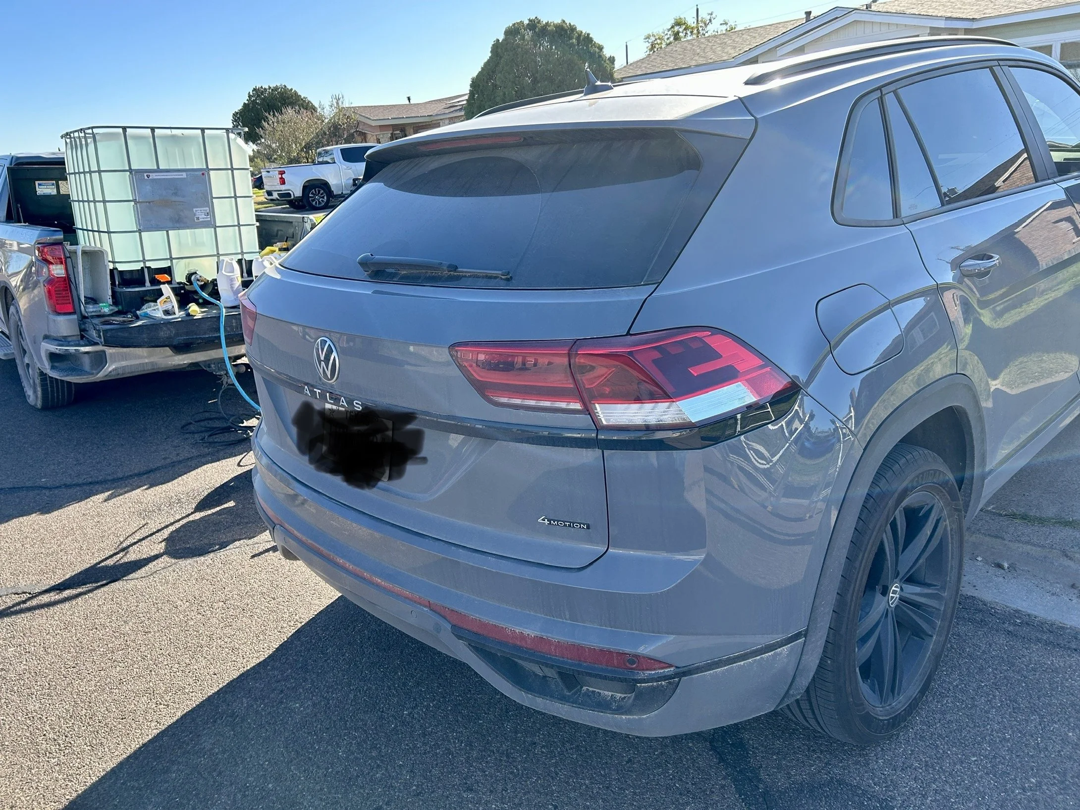 A gray Volkswagen Atlas SUV parked in a driveway connected to a portable power station on a pickup truck via an extension cord.