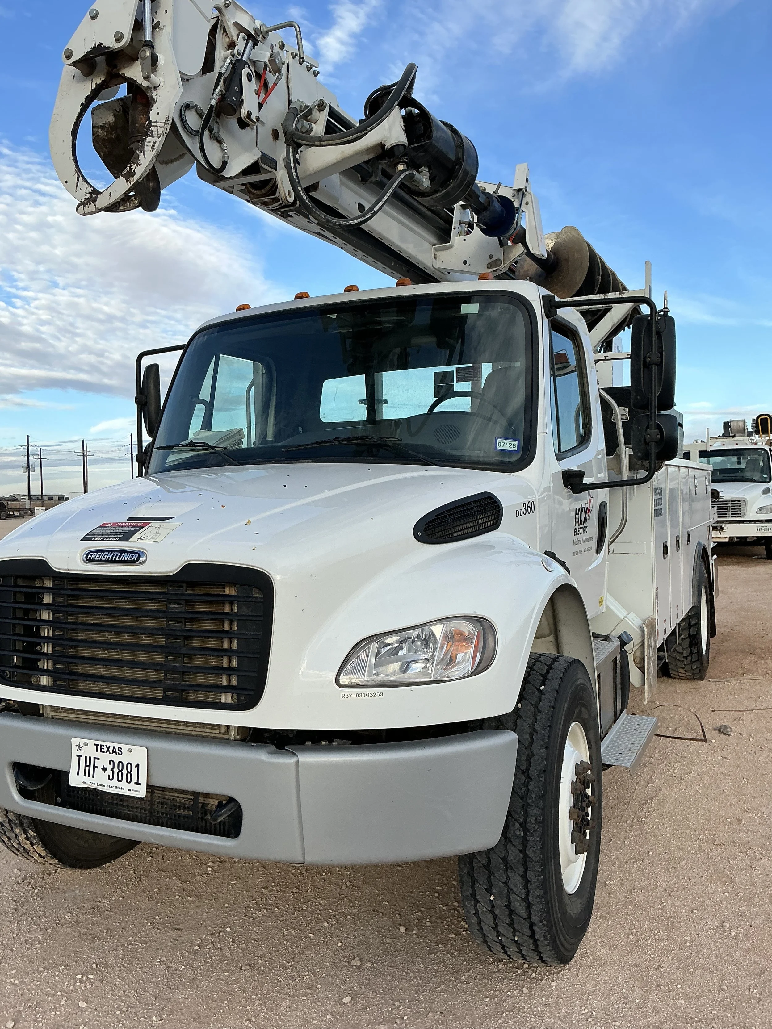 White utility truck with a bucket lift on the roof, parked on a dirt lot under a partly cloudy sky in Texas.