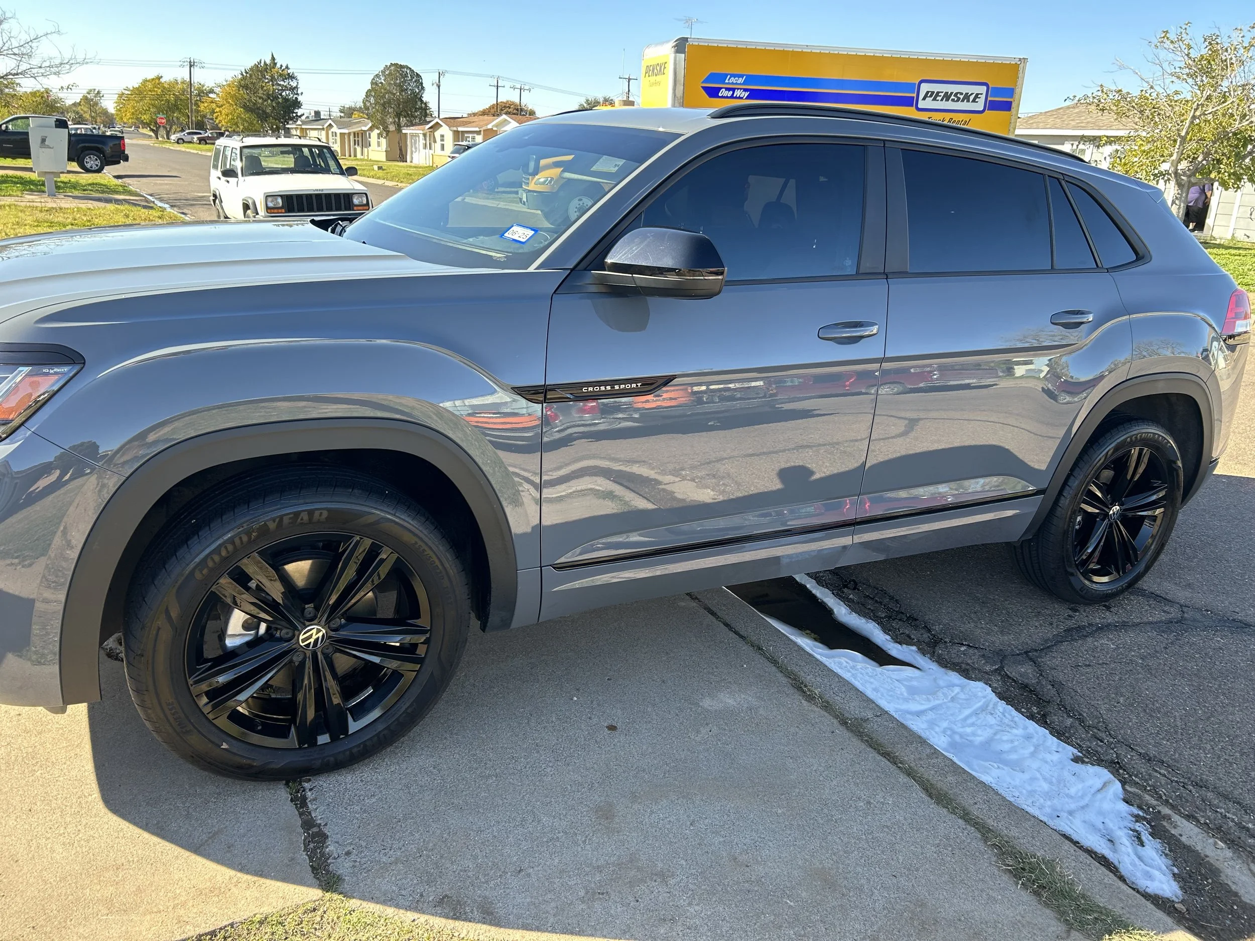 Grey Volkswagen SUV parked on a curb with snow on the sidewalk and other vehicles in the background under a blue sky.