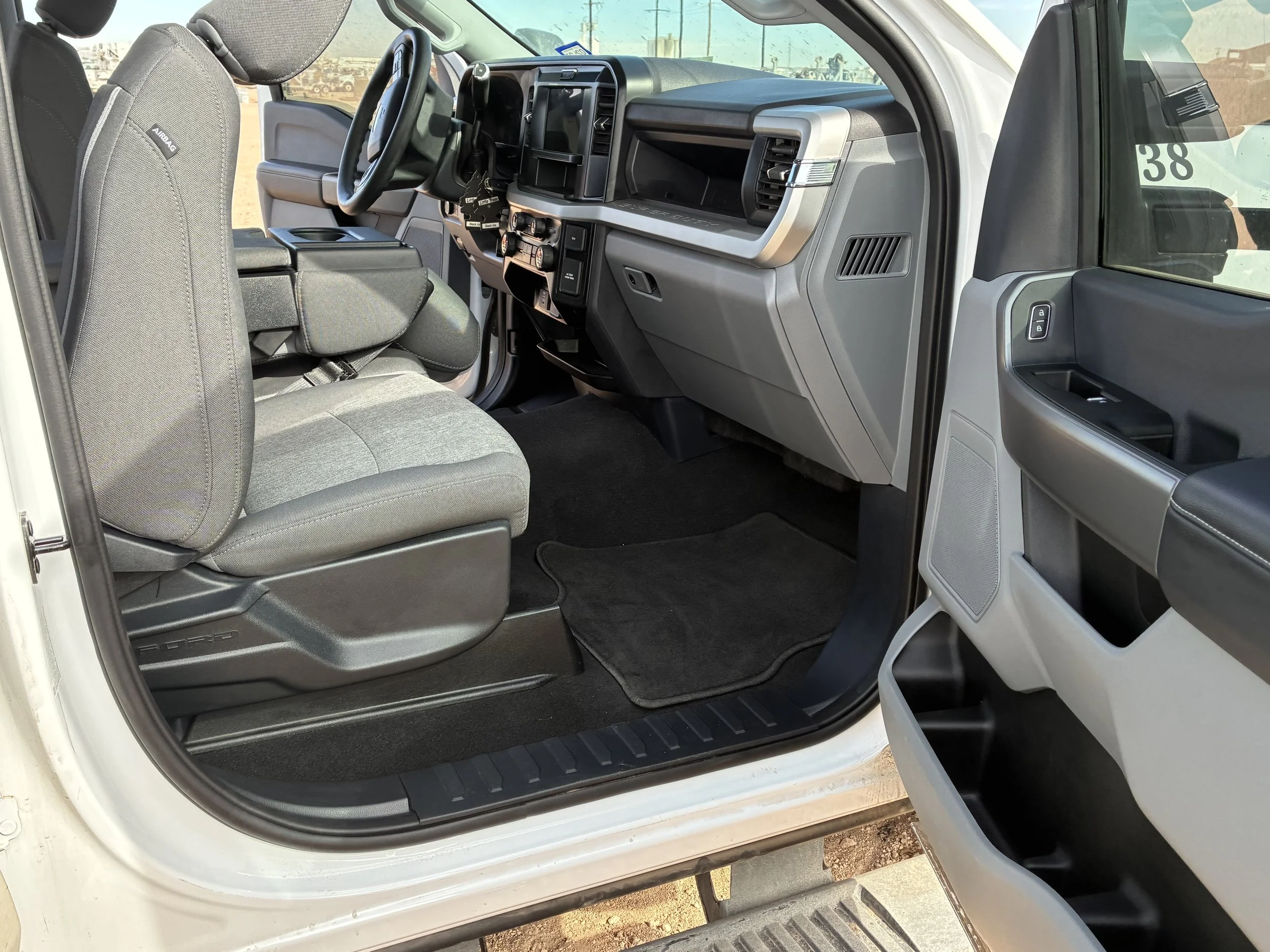 Interior of a pickup truck showing gray passenger seat, black floor mats, dashboard with controls, and part of the driver's side door.