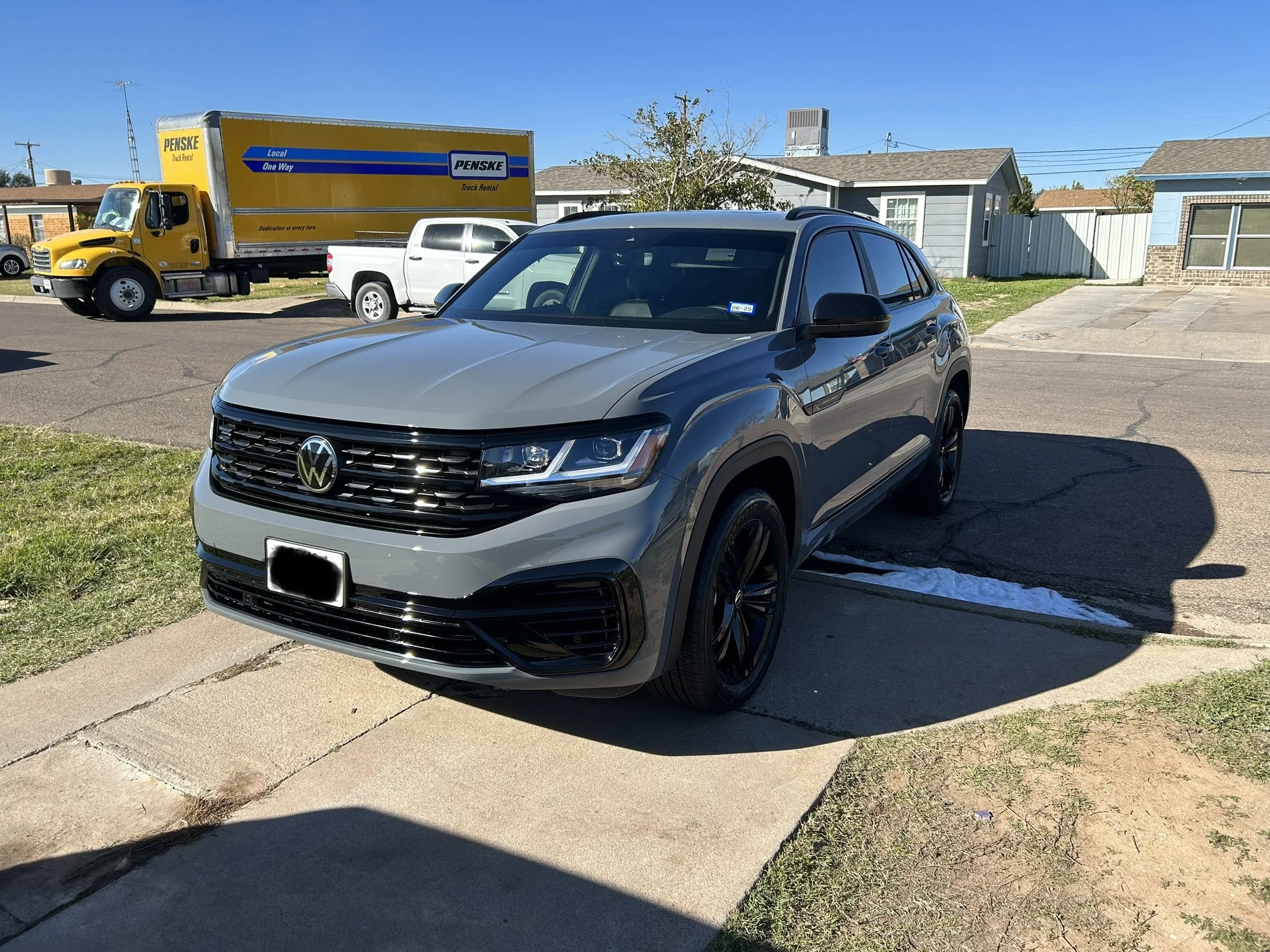 Gray Volkswagen SUV parked on a driveway in a residential neighborhood under clear blue sky.