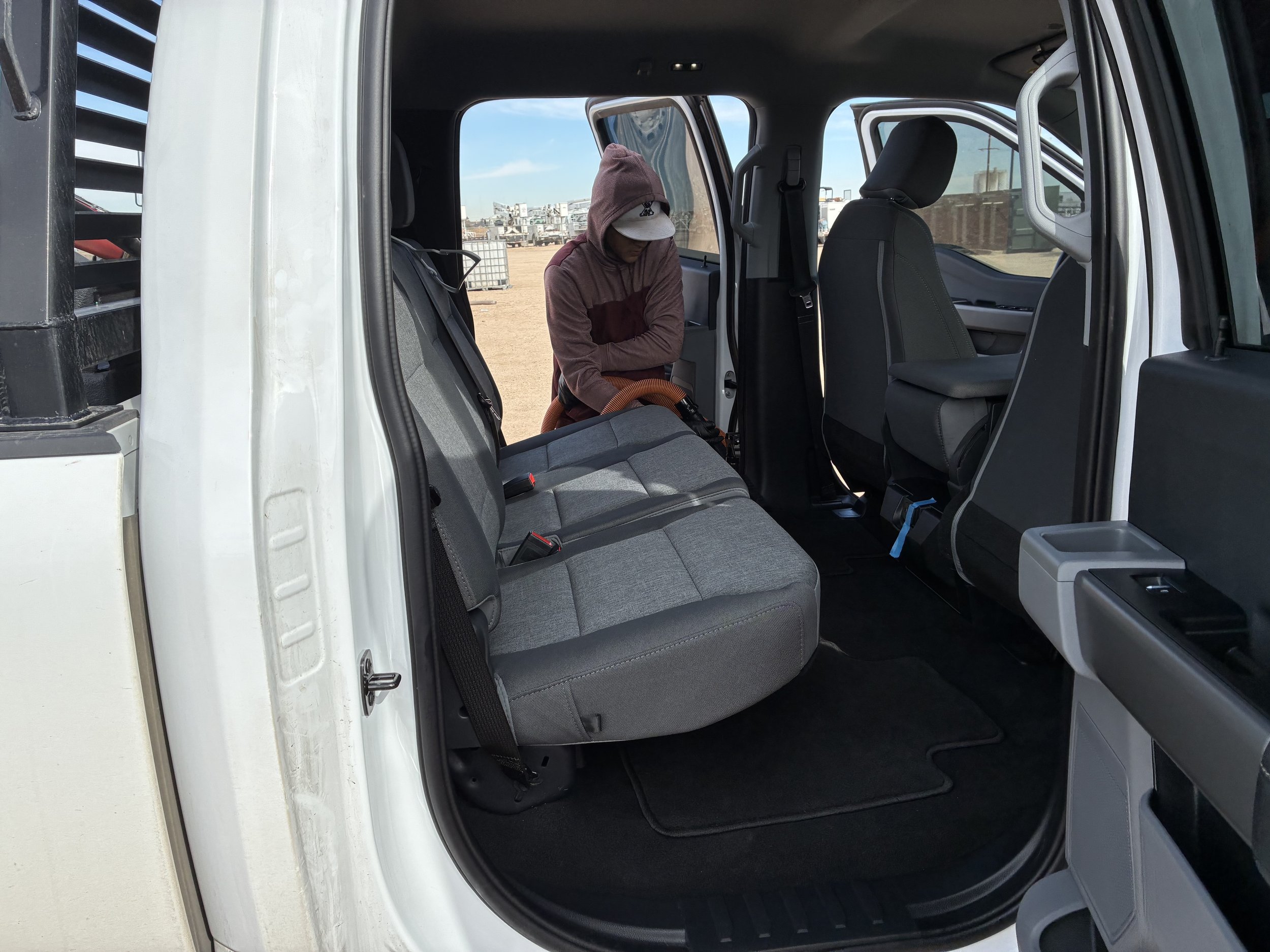 Person in a hoodie cleaning the back seat of a white pickup truck.