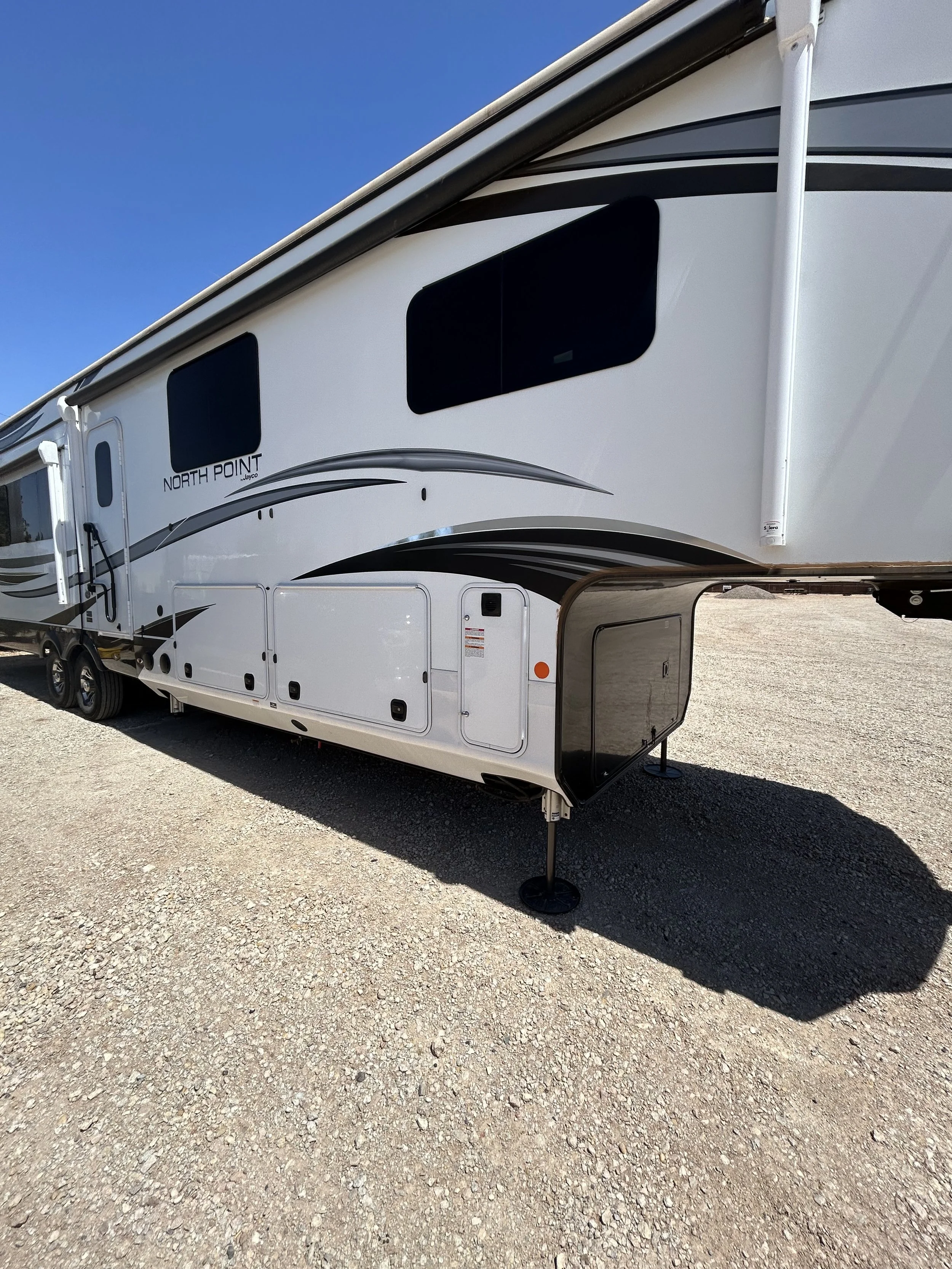 A white Jayco North Point fifth wheel RV parked on a gravel lot with a clear blue sky in the background.
