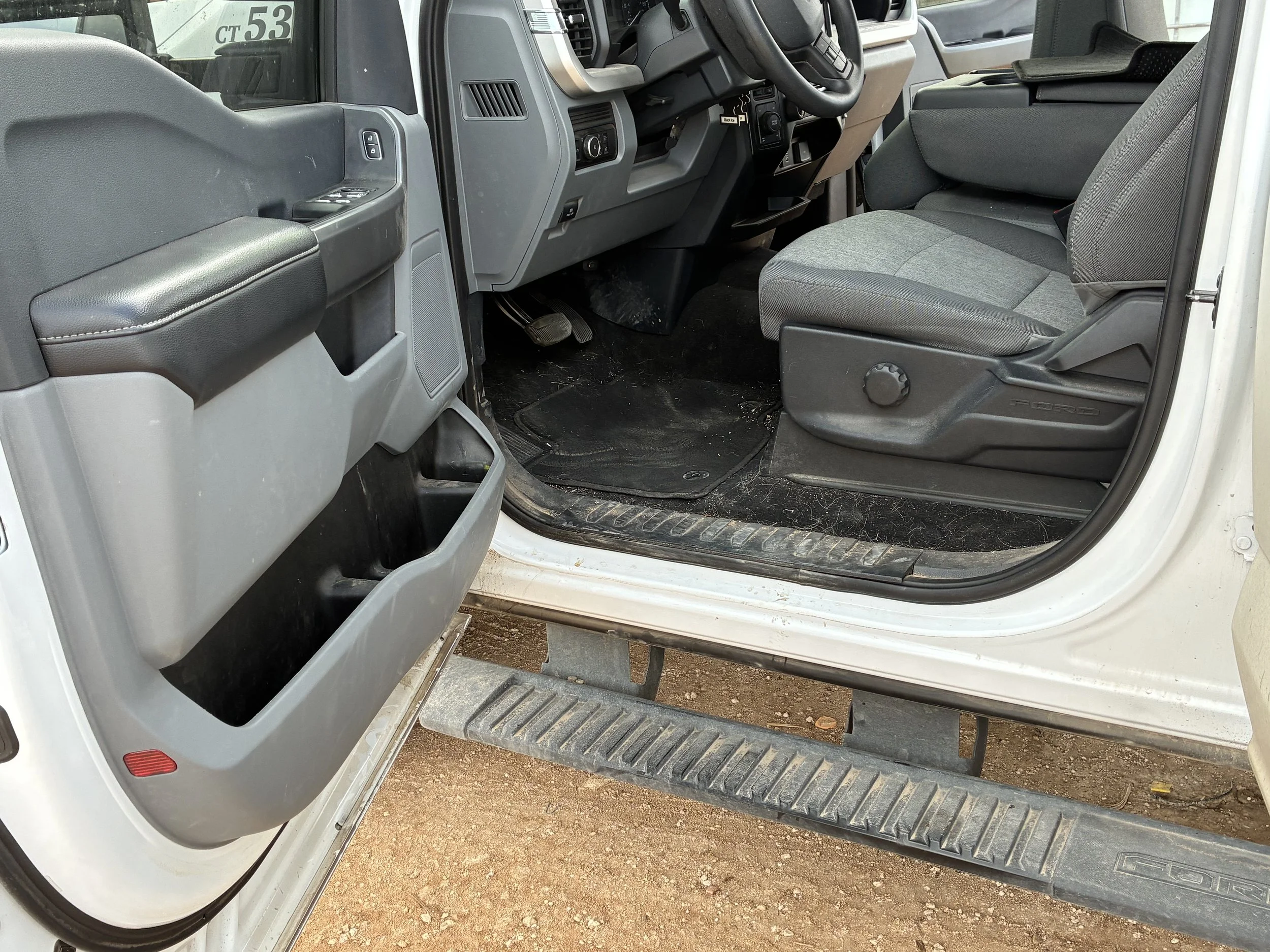Interior of a pickup truck showing the driver's seat, dashboard, and open passenger door with storage compartments.