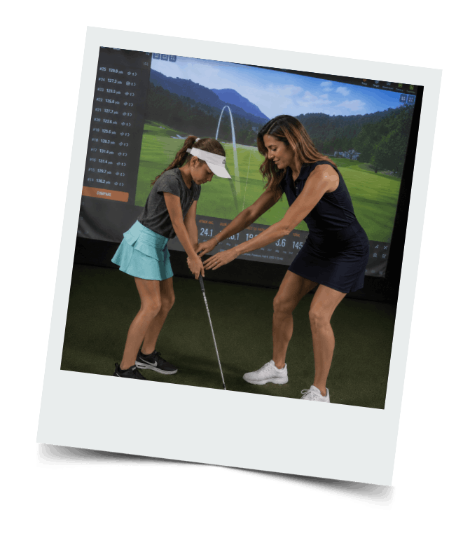 Coach with golfing student at indoor golfing range.