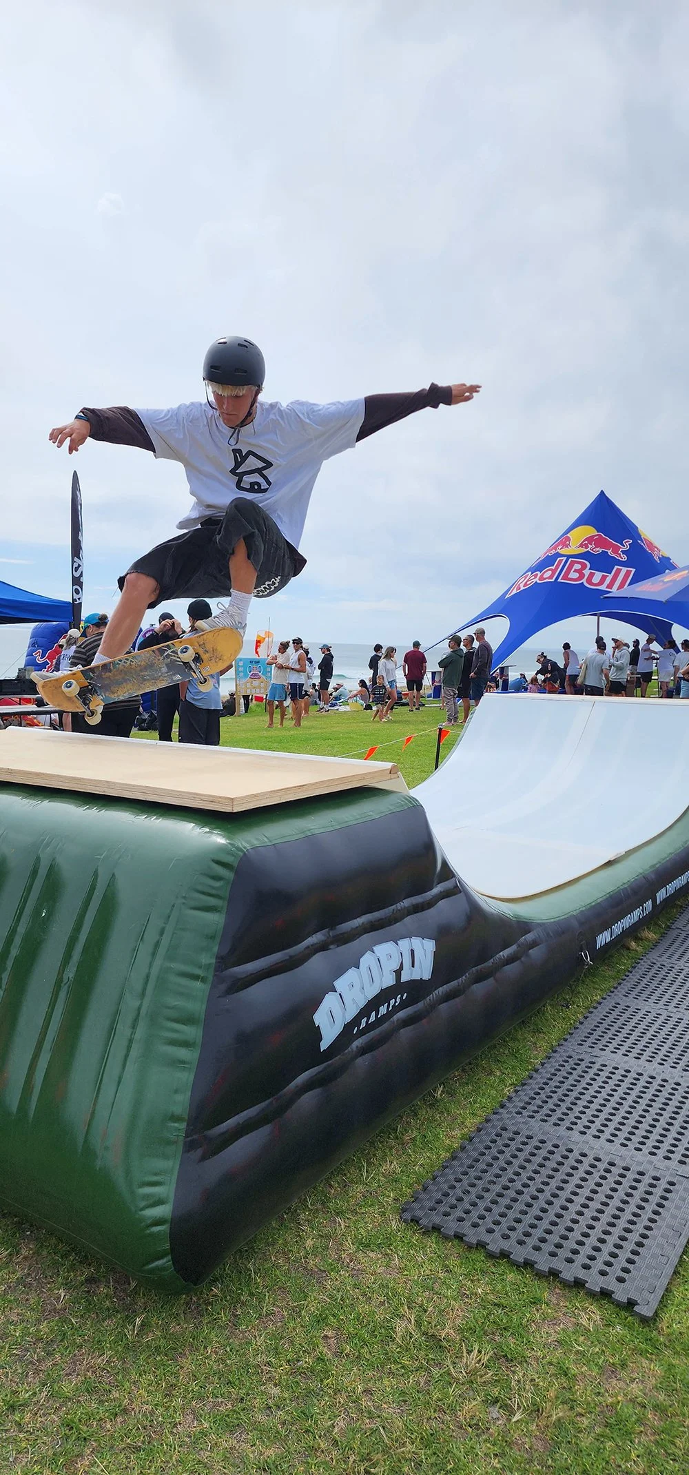 Skateboarder in mid-air performing a trick on a ramp at an outdoor event.
