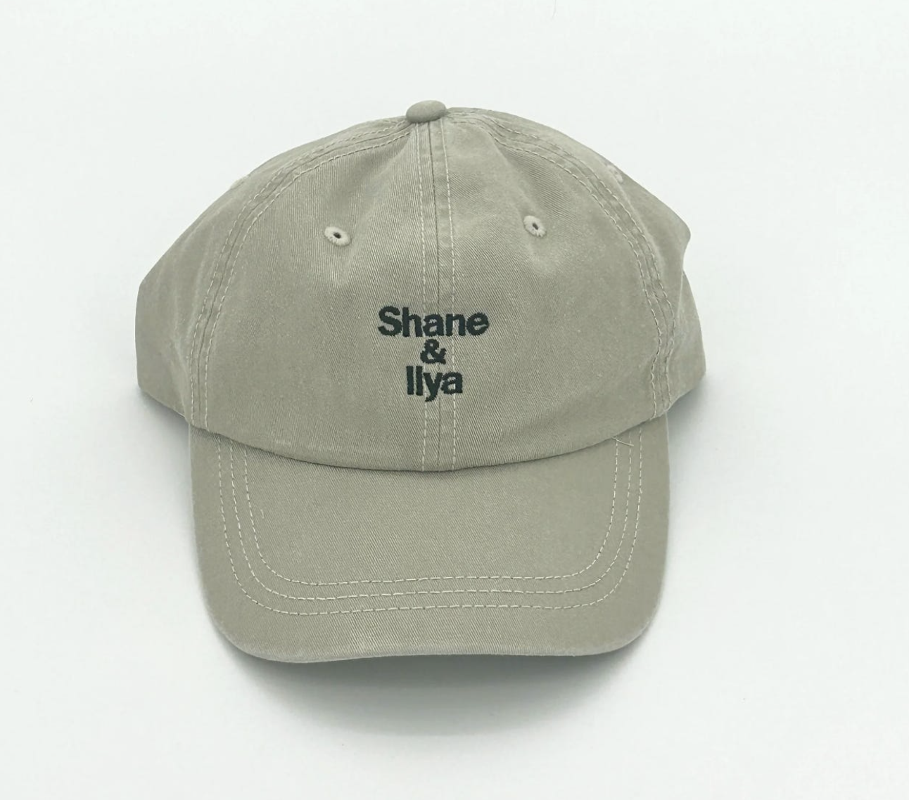Beige baseball cap with embroidered text 'Shane & Ilya' on the front.