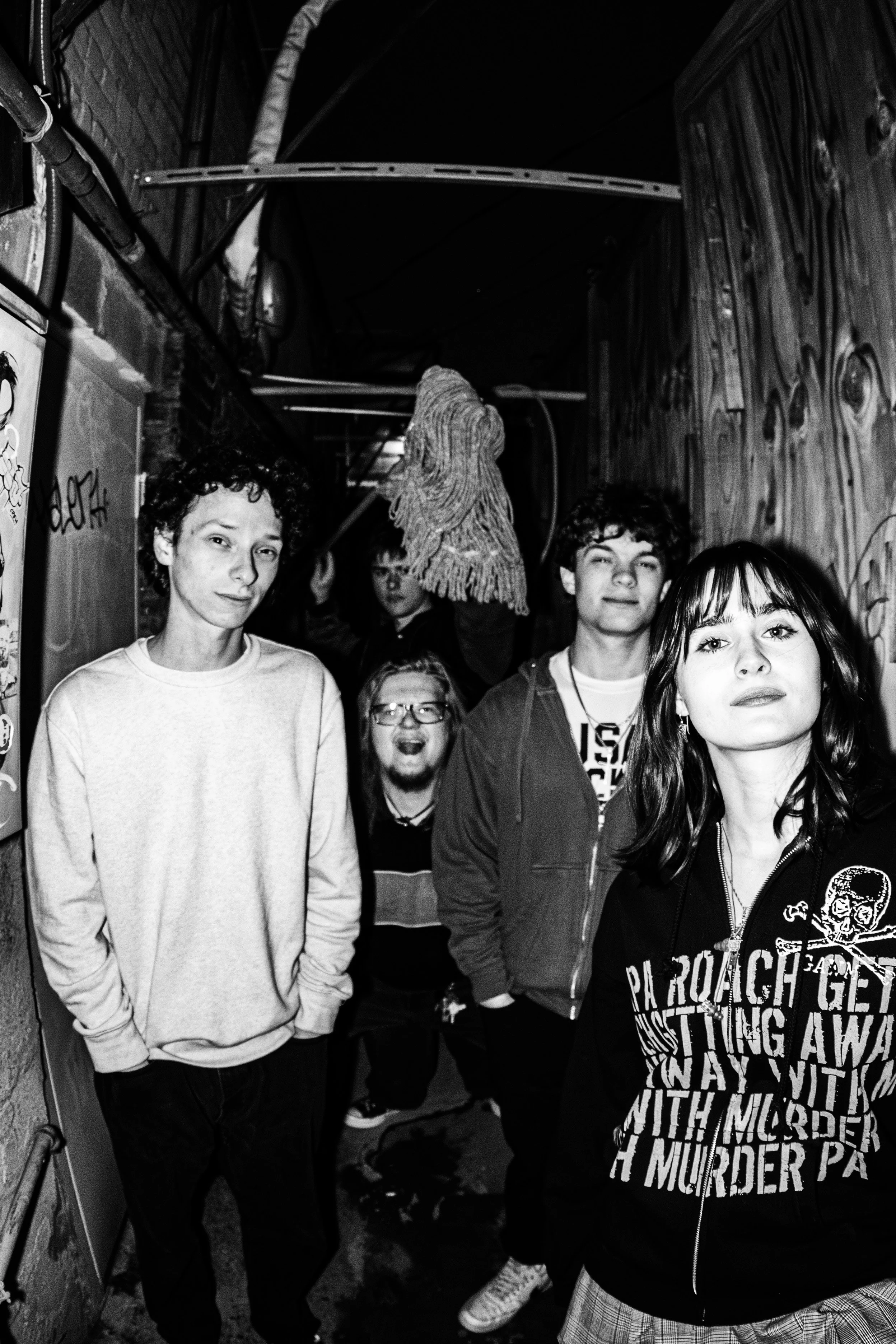 A group of five young people in an alleyway, with graffiti on the wall, black and white photo, casual clothing, and an expressive, rebellious attitude.