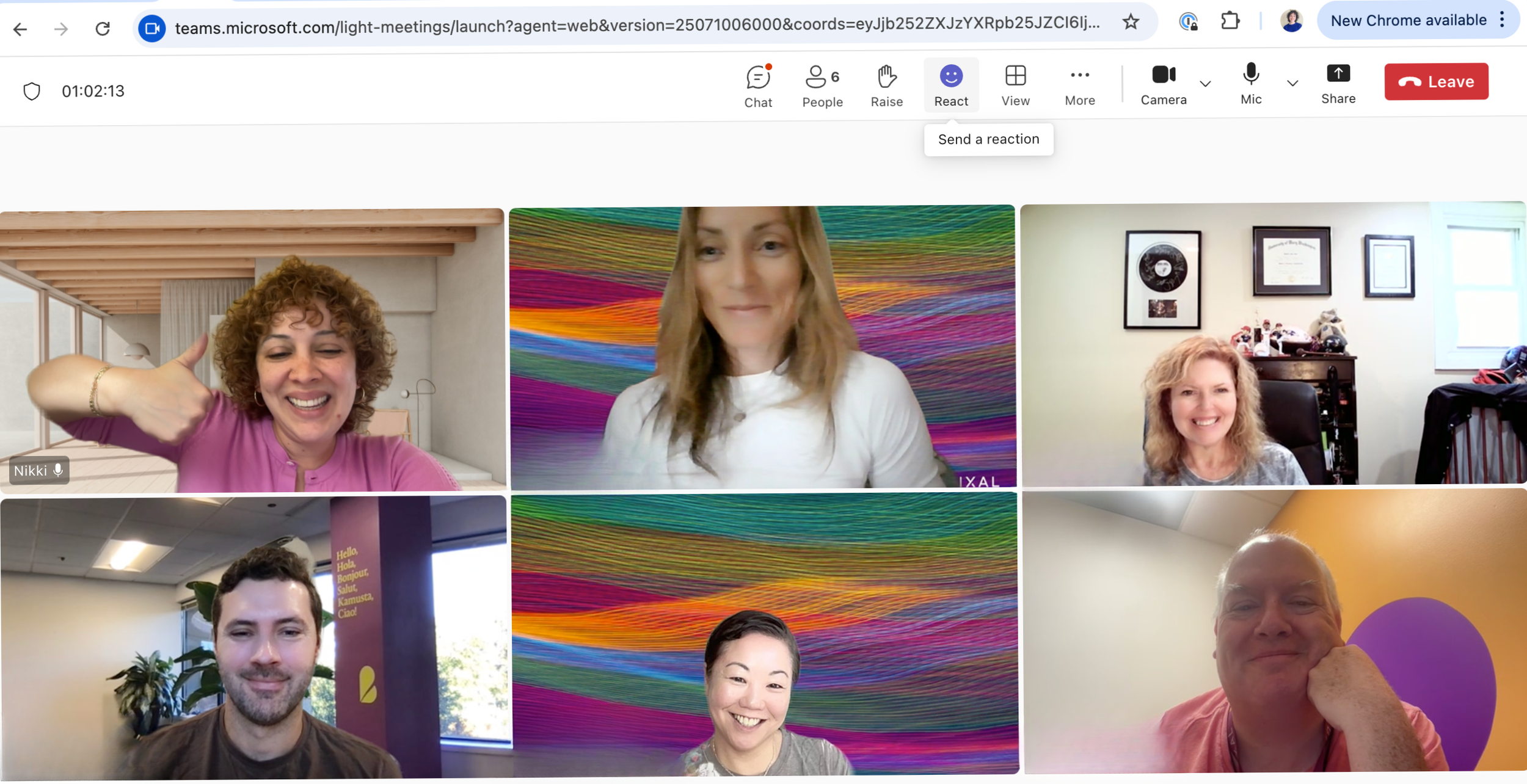 Six people in a virtual video call, smiling and posing for the camera, with assorted backgrounds including a colorful textile wall, framed pictures, and office spaces.
