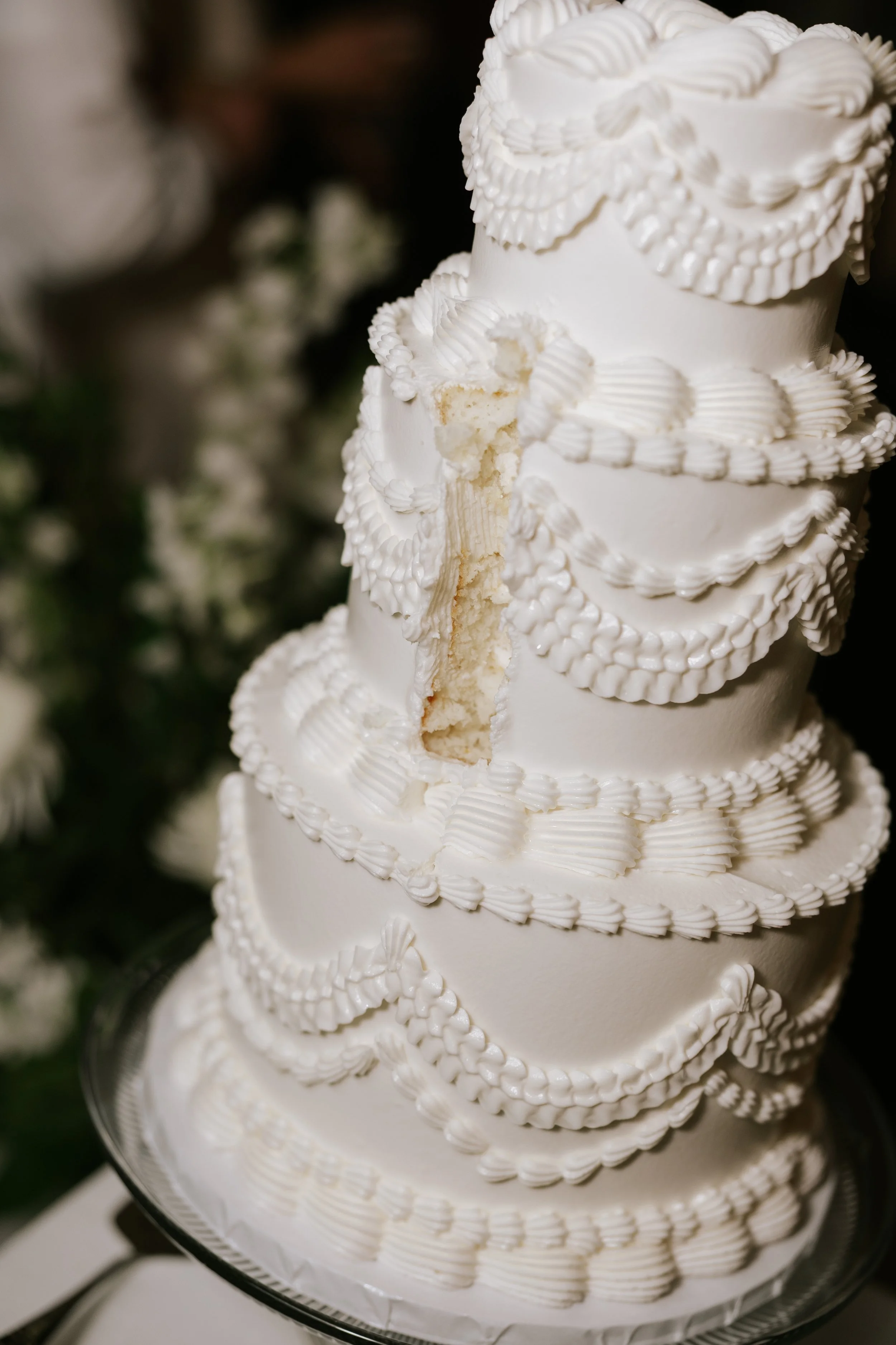 A multi-tiered wedding cake decorated with white frosting swirls and piping, with a bite taken out of the middle tier, revealing vanilla cake layers inside.