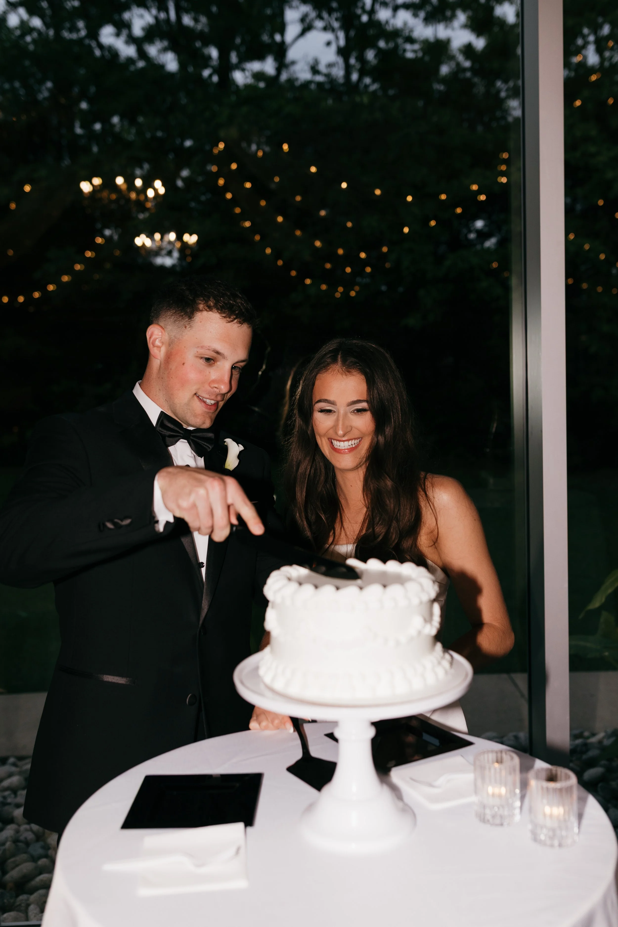 A newlywed couple in formal attire cutting a wedding cake at a reception.