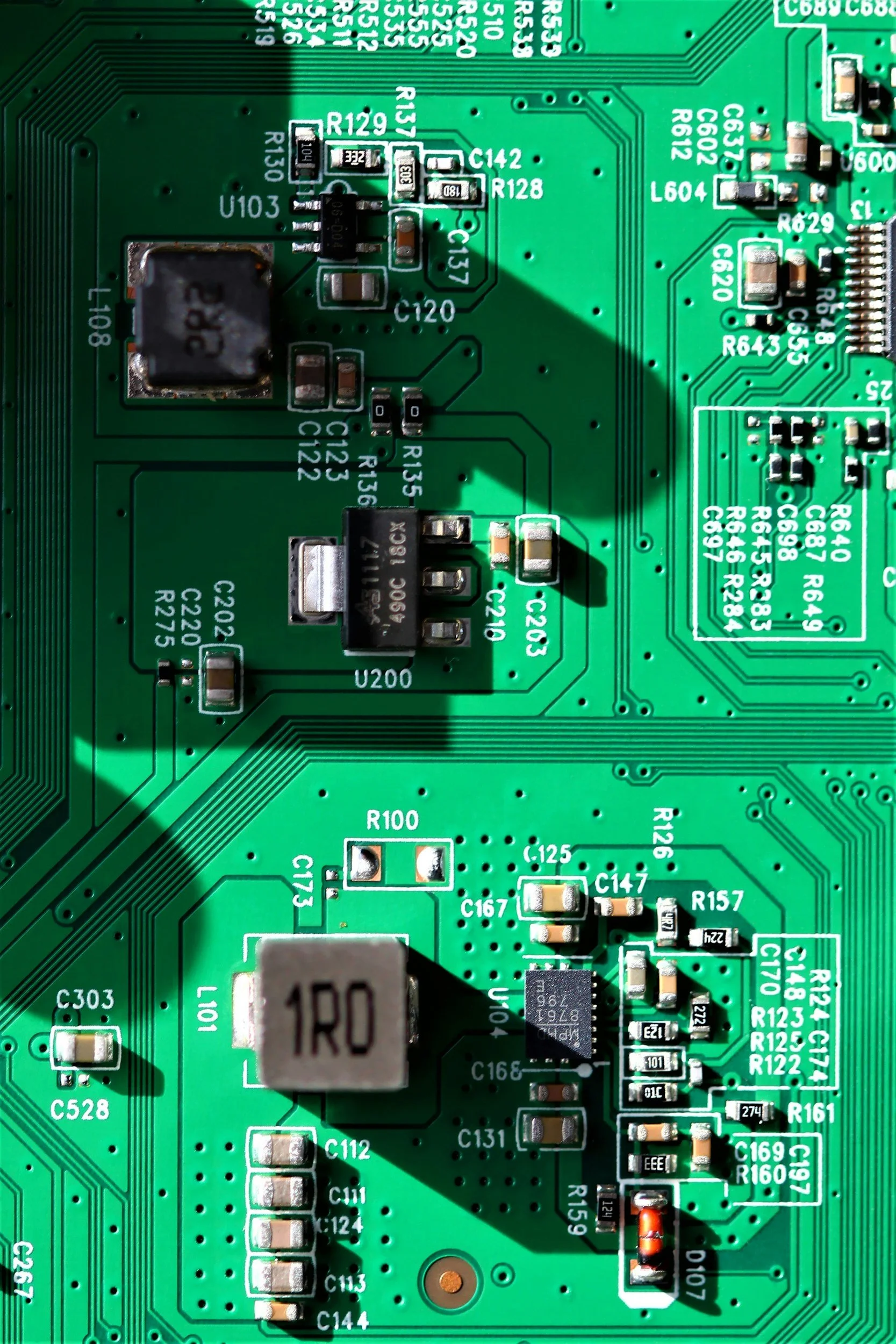 Close-up of a green printed circuit board with electronic components, including resistors, capacitors, and integrated circuits, labeled with white print.