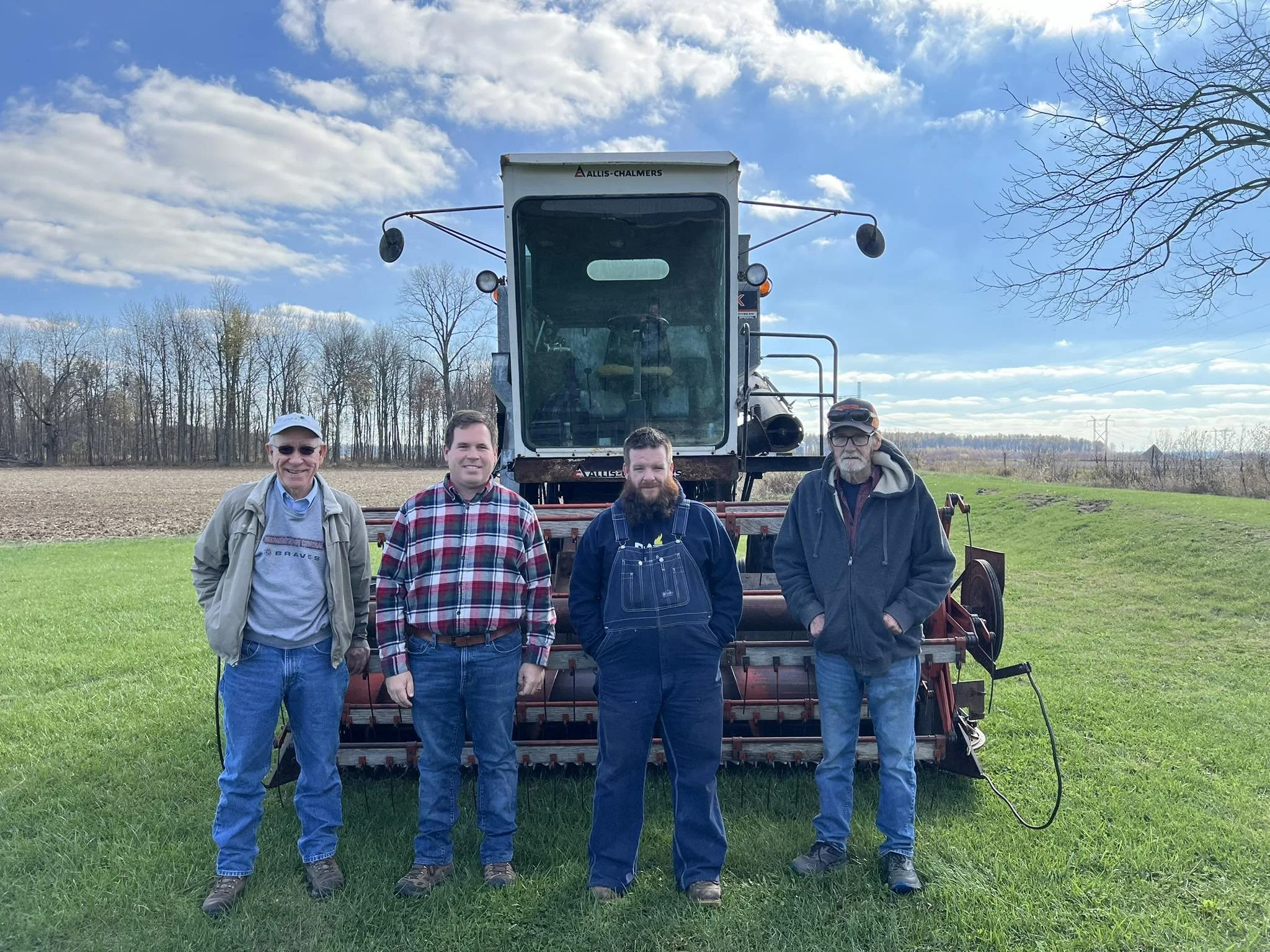 Four men standing in front of a large green harvesting machine on a farm field.