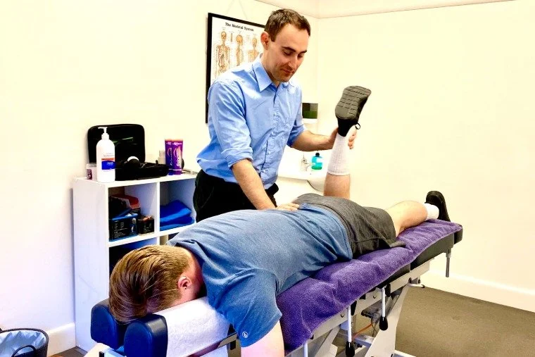 Chiropractor performing a spinal adjustment on a patient lying face down on an adjustment table in a medical office.