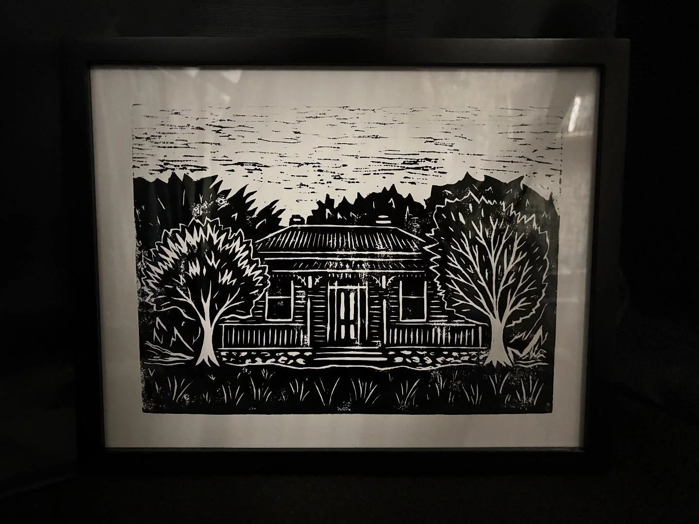 Silhouette of a house with a porch, two trees on either side, and trees and clouds in the background, all in black and white.