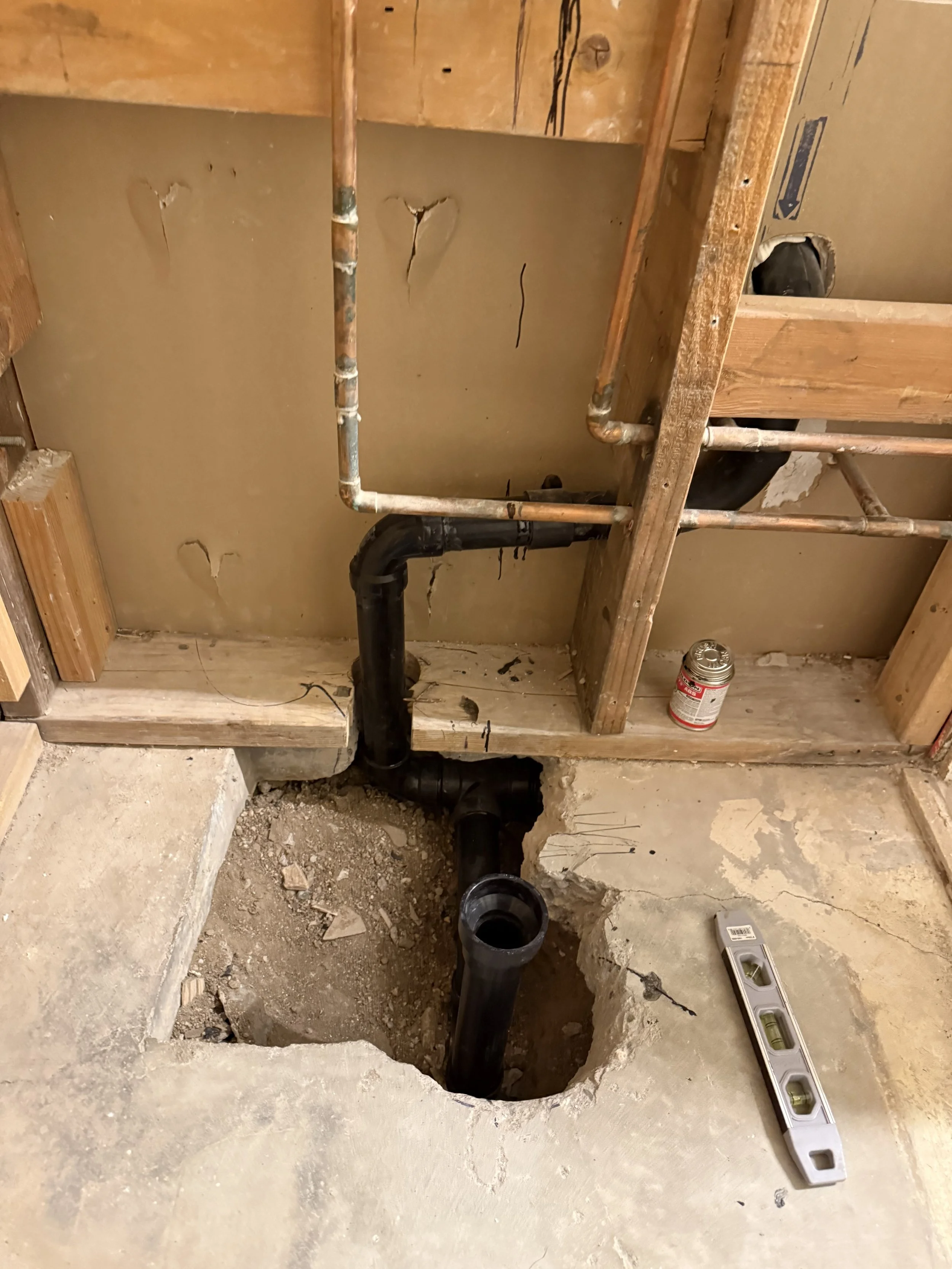 Plumbing pipes installed in a construction site with a level tool on the floor and a hole in the concrete for pipe installation.