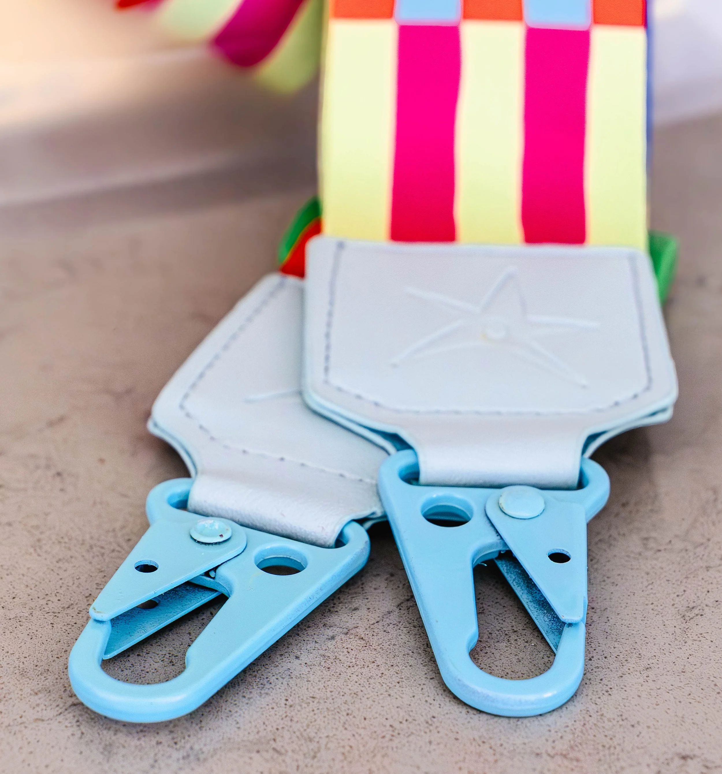 Close-up of two toy claw clips attached to a piece of fabric, with background of a colorful striped object.