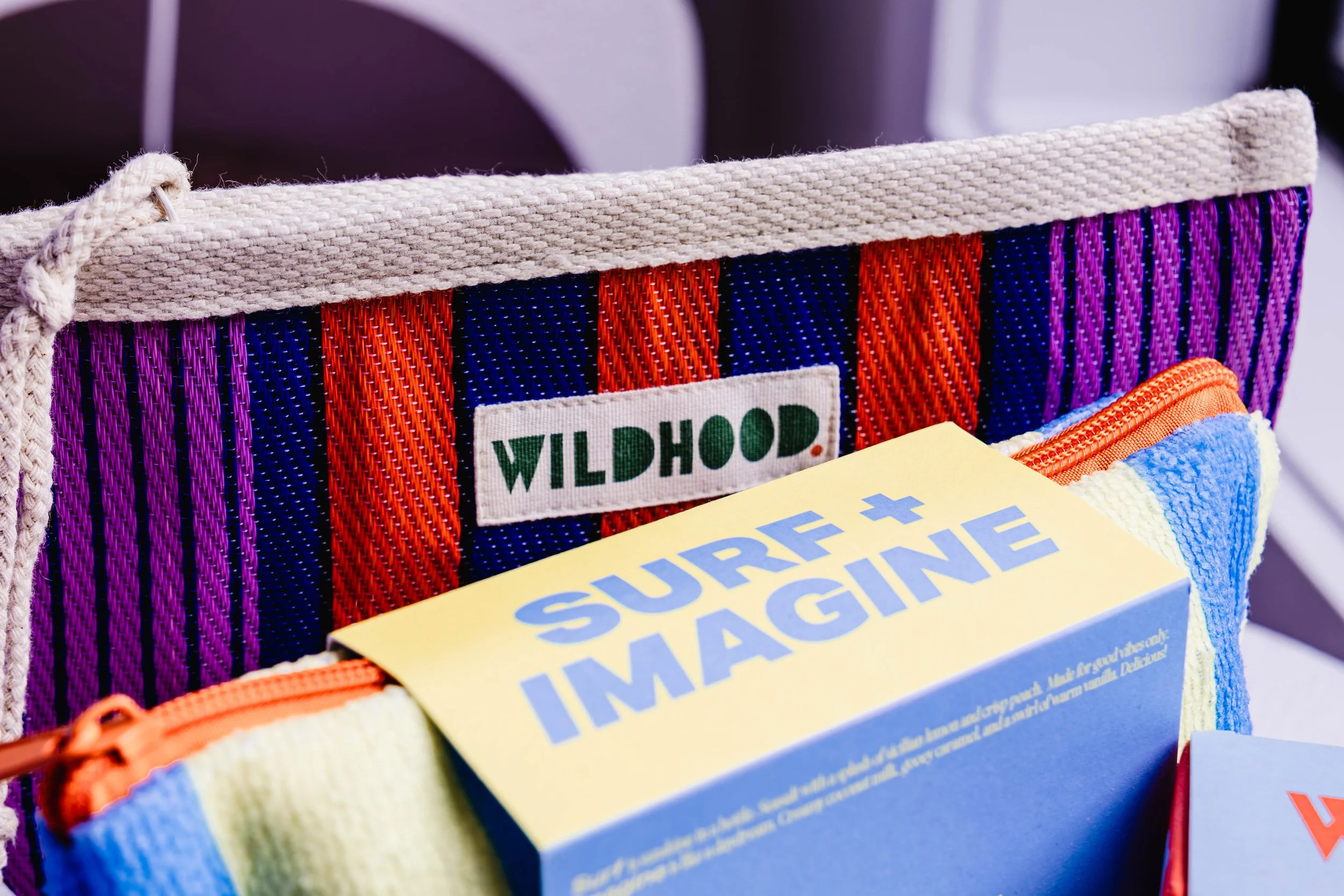 Close-up of colorful striped fabric bag with a label that says 'Wildhood' and a yellow box labeled 'Surface + ImaginE' inside.