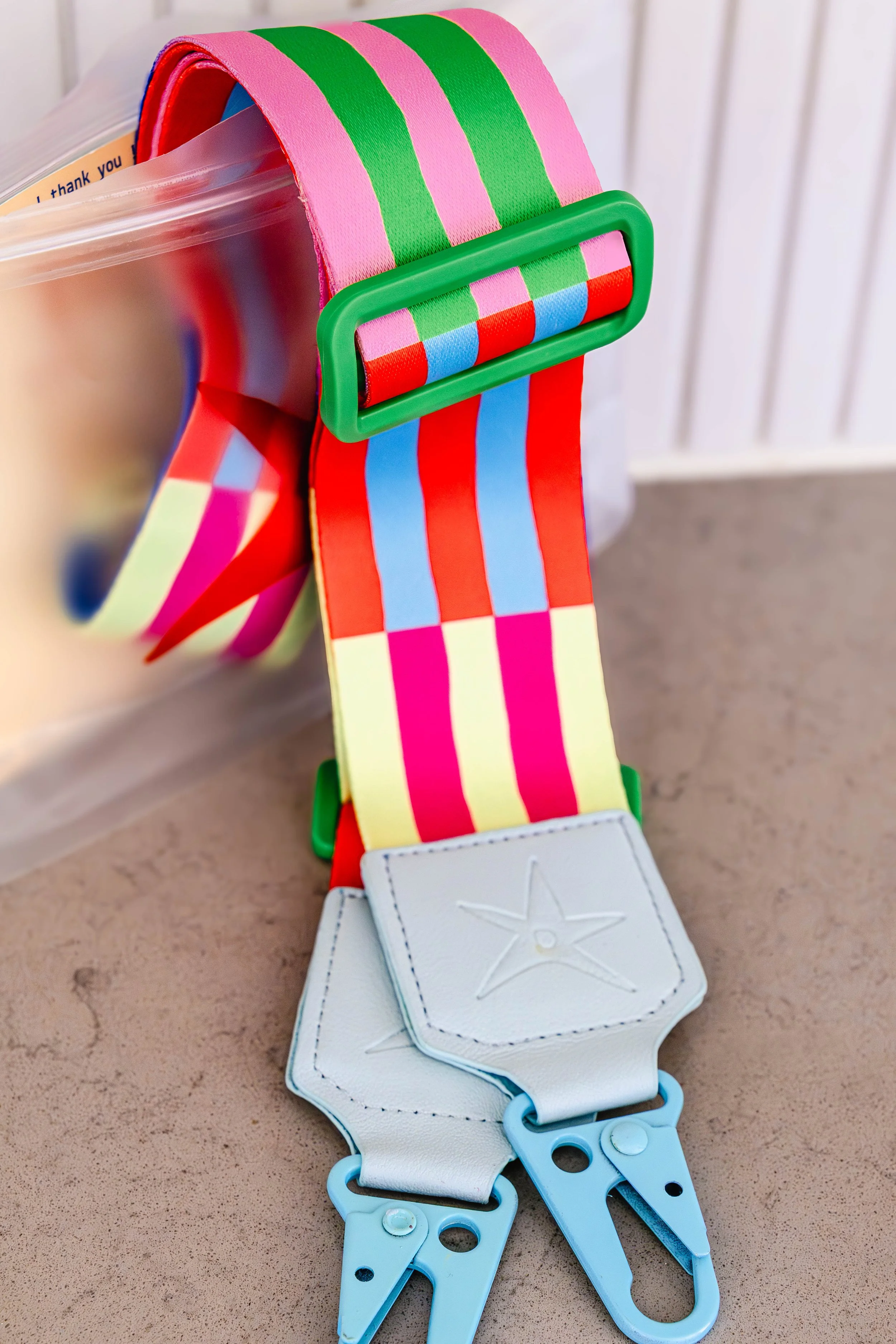 Close-up of a colorful striped strap with a star design, attached to a white leather-like holder with metal clips.