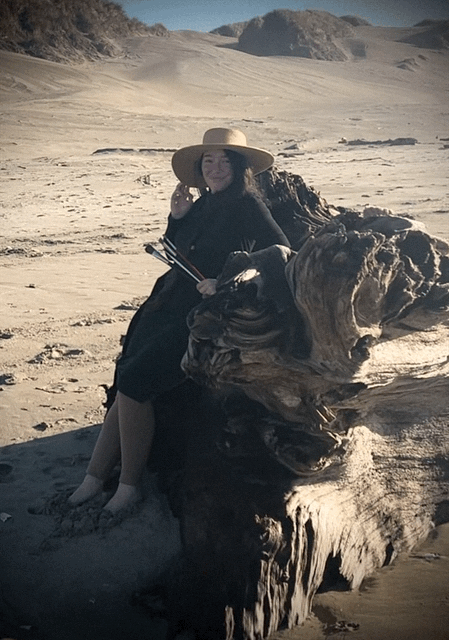 Artist in her element, sitting on driftwood on a sandy beach gathering inspiration.