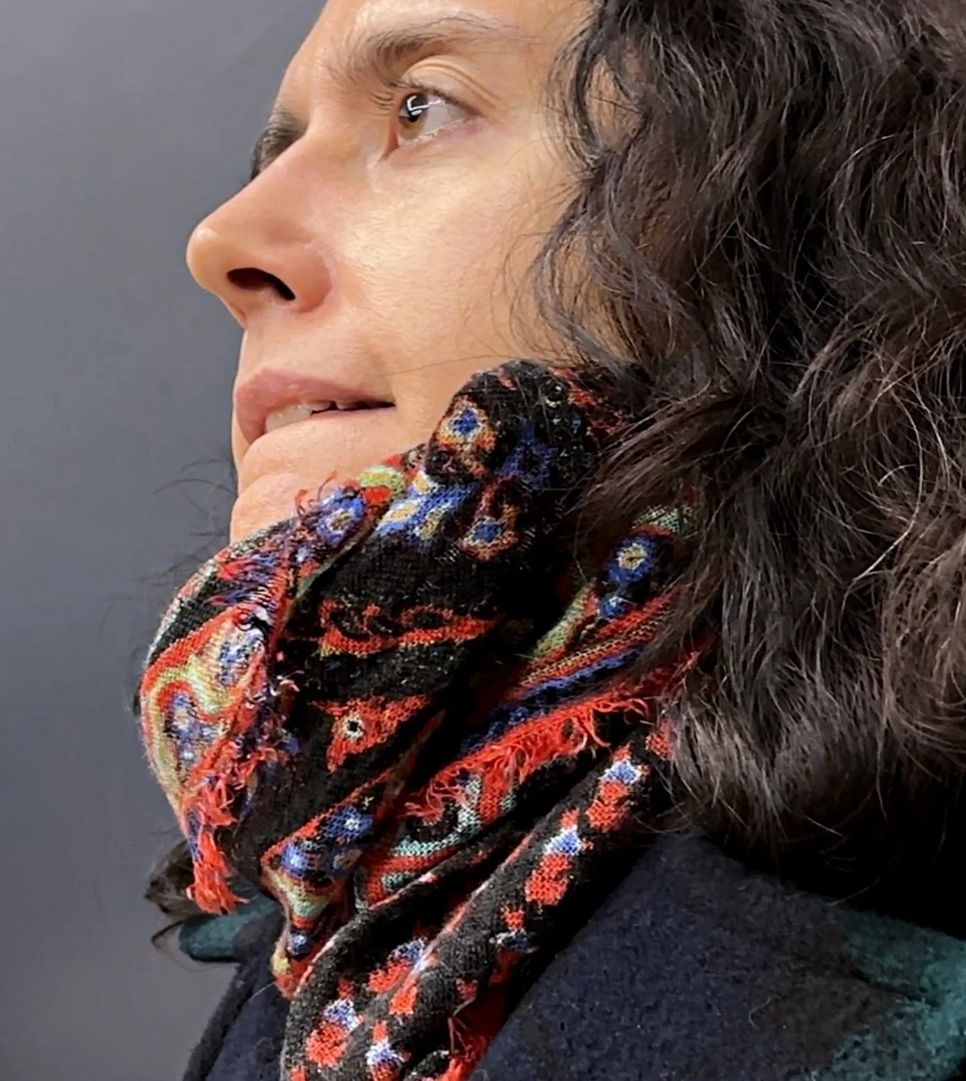 Close-up of a woman with wavy brown hair wearing a colorful patterned scarf around her neck, facing sideways. This is Christina Masciotti author of Liberty Scrap premiering at Culture Lab LIC in March 2026.