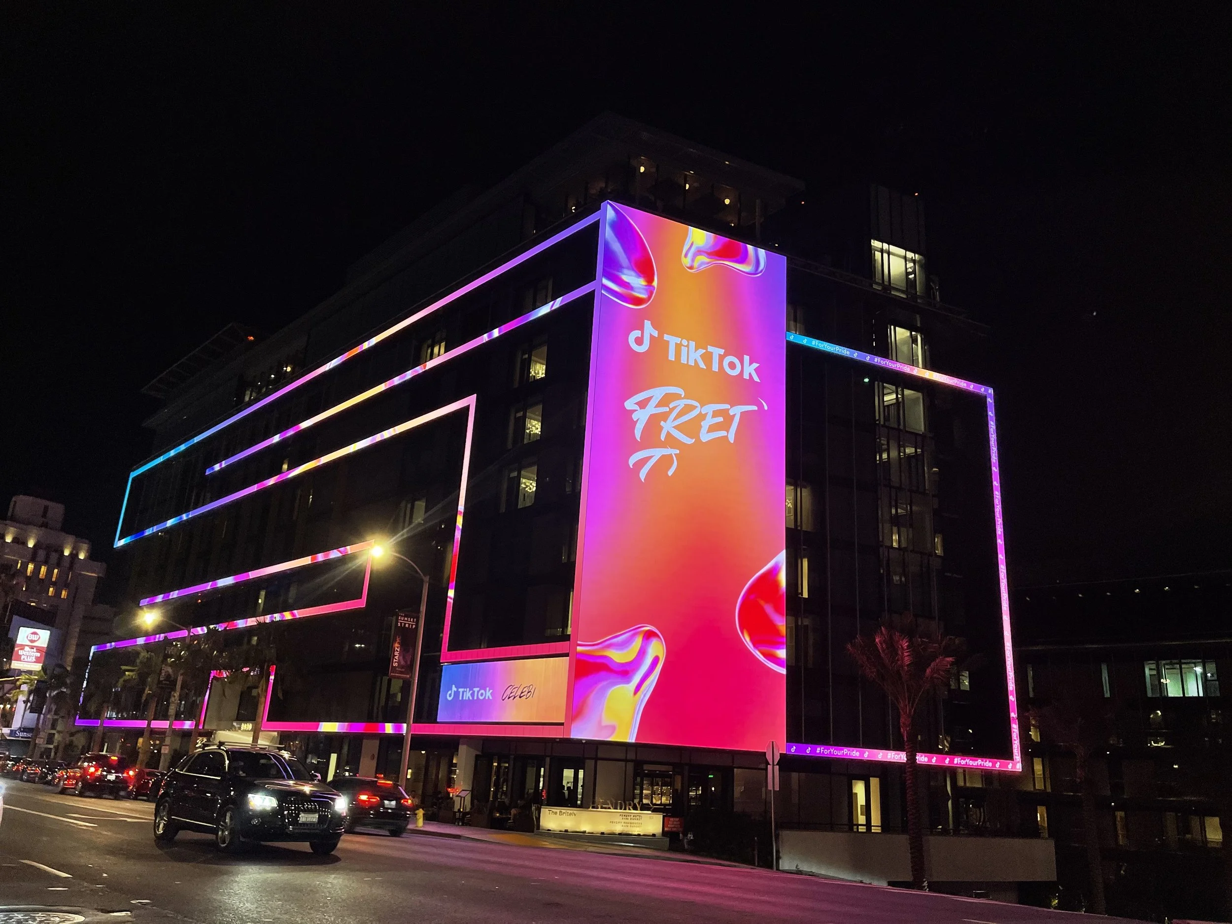 Night view of a modern building with colorful, neon-illuminated rectangular outlines and a large digital billboard displaying TikTok branding and a vibrant background.
