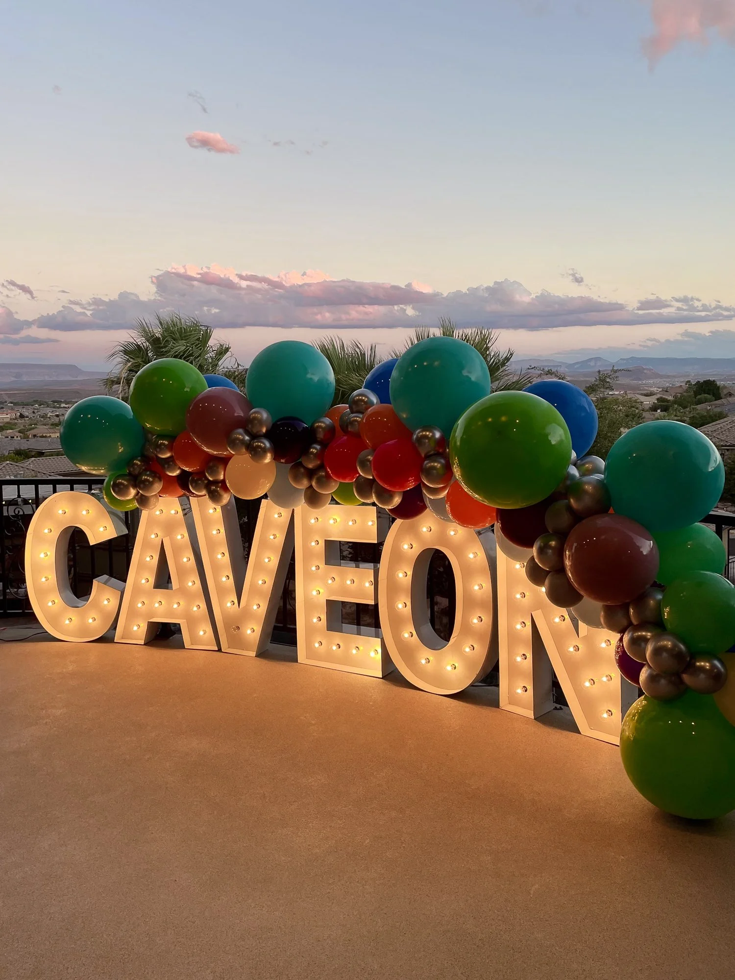 Decorative balloons arranged around large illuminated letters spelling 'CAV