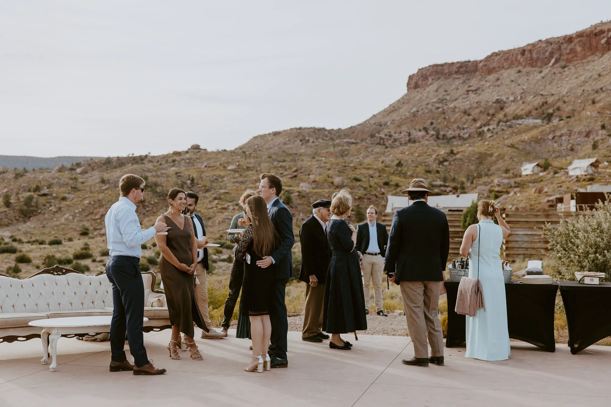 Group of people gathered outdoors at a desert wedding or event, with a mountain landscape in the background.
