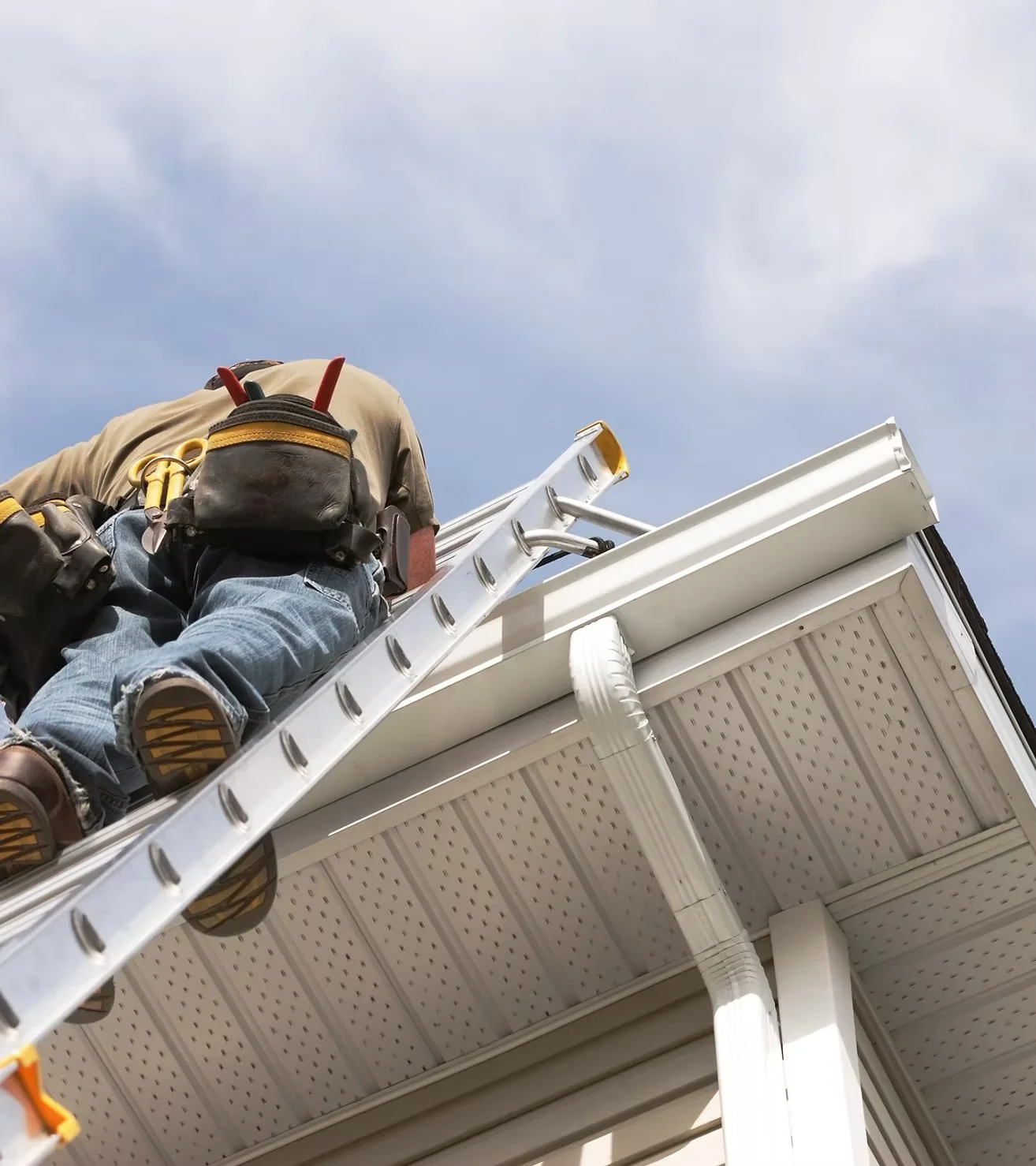 A person working on the roof of a house, standing on an extension ladder against the house's eaves, with tools and a backpack, under a partly cloudy sky. Blackwater Ridge covers all of your maintenance needs on campus.