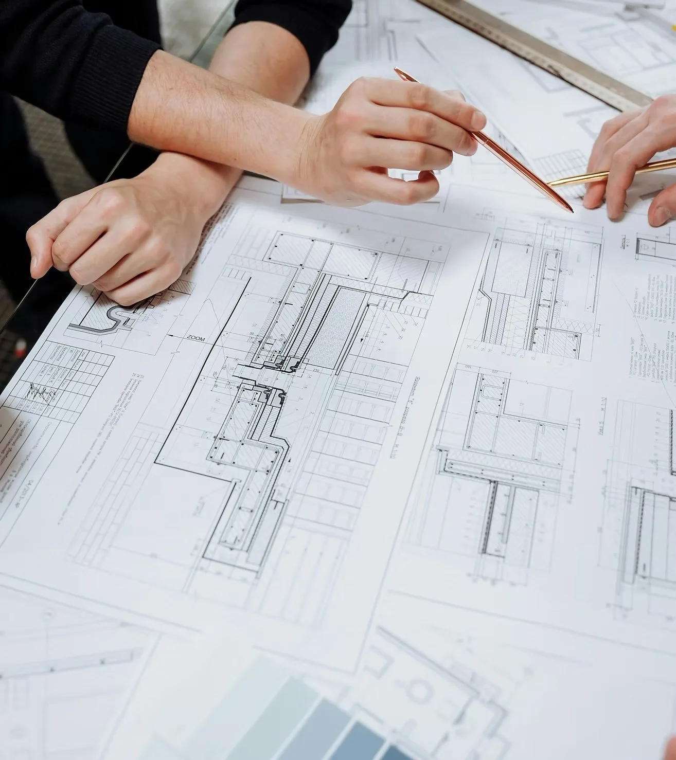 Two people examining and discussing architectural blueprints on a table, with one person pointing a pen at the plans.
