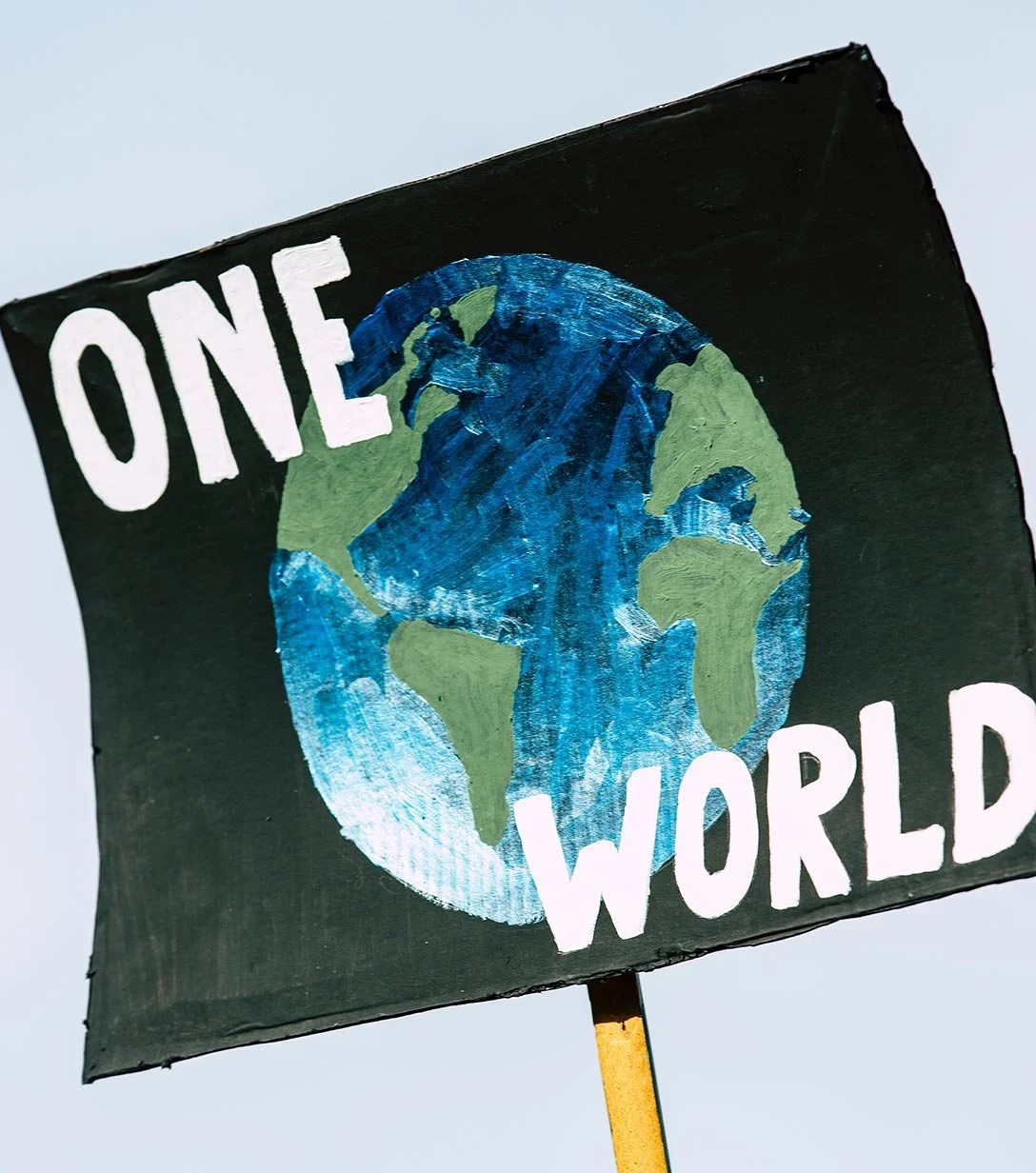 A sign featuring a painted Earth with the words "ONE WORLD" on a black background.